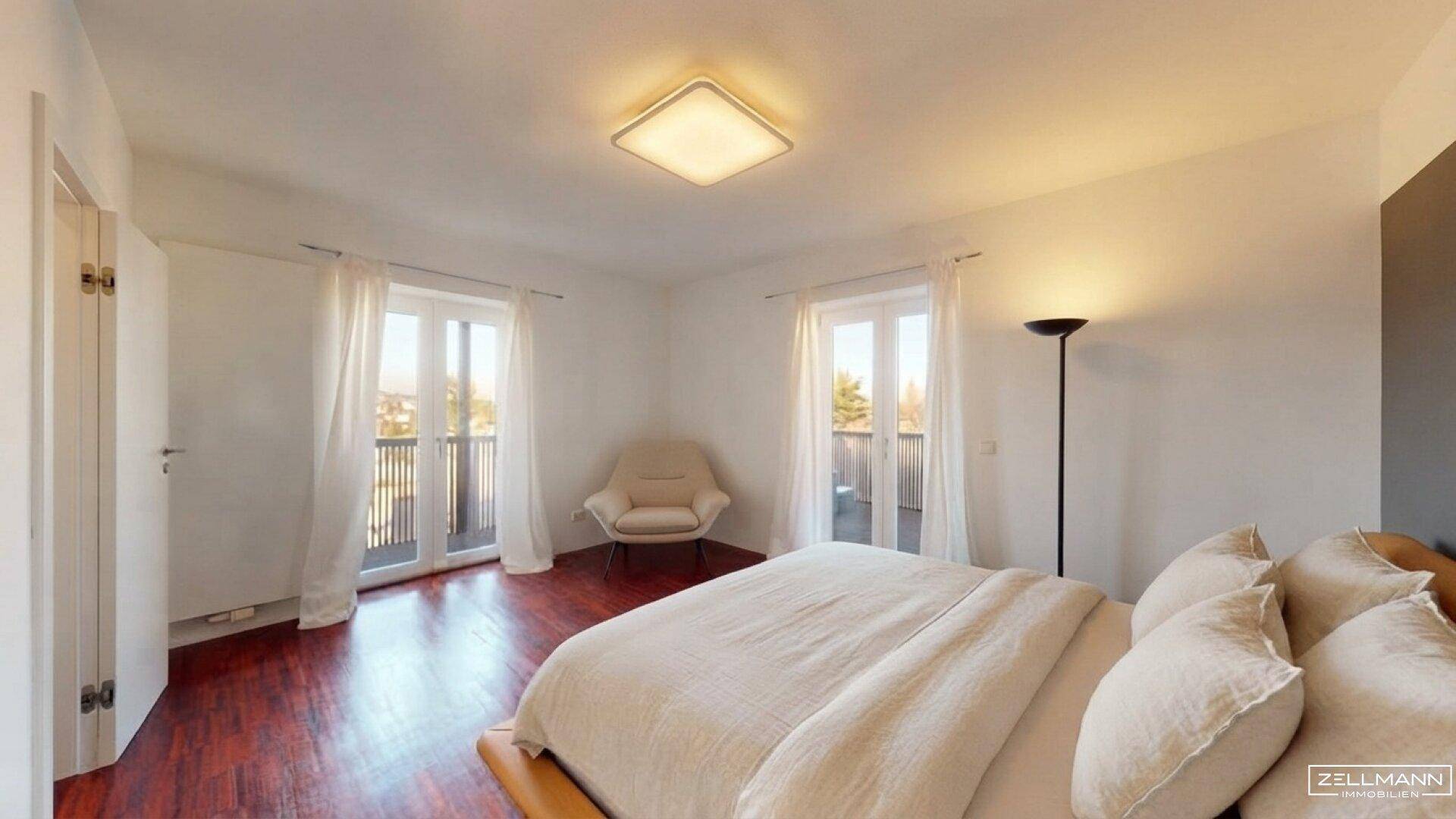 Schlafzimmer mit Holzboden, hellem Bett und Zugang zu zwei Balkonen.