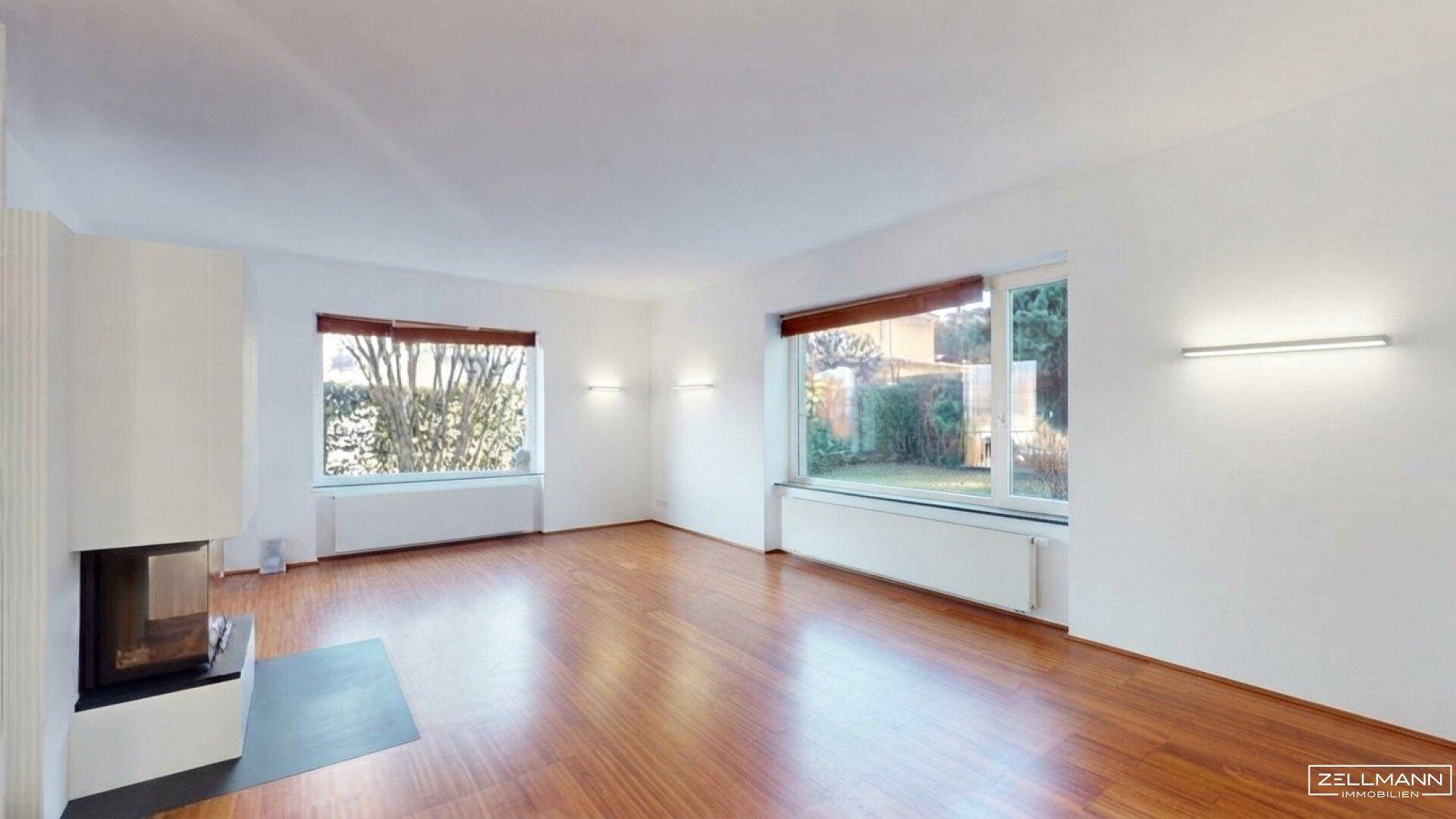 Geräumiges Wohnzimmer mit Kamin, Holzboden und großen Fenstern zum Garten.