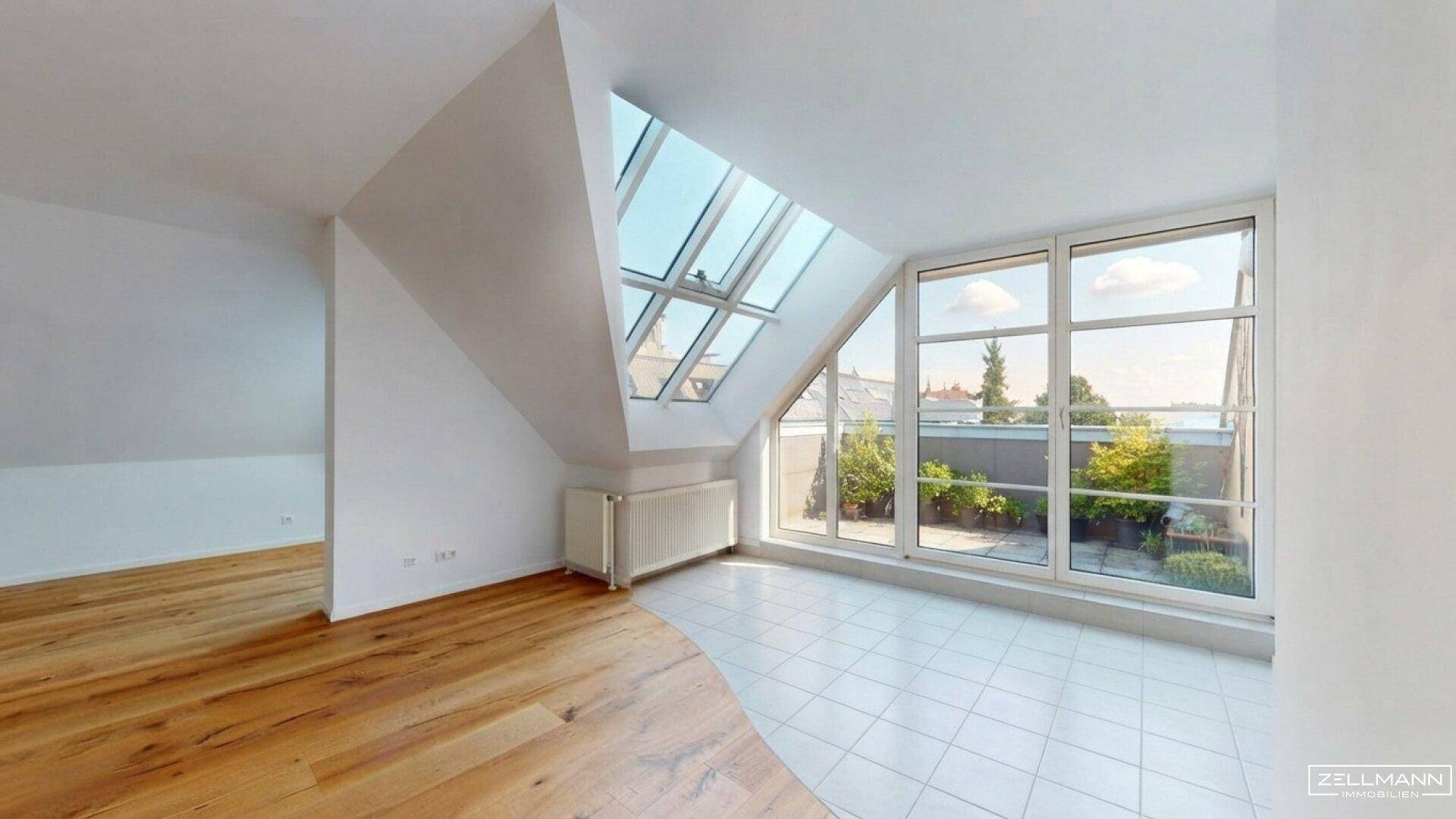 Heller, leerer Raum im Dachgeschoss mit großen Fenstern, Dachschrägen und zwei Bodenbelägen.
