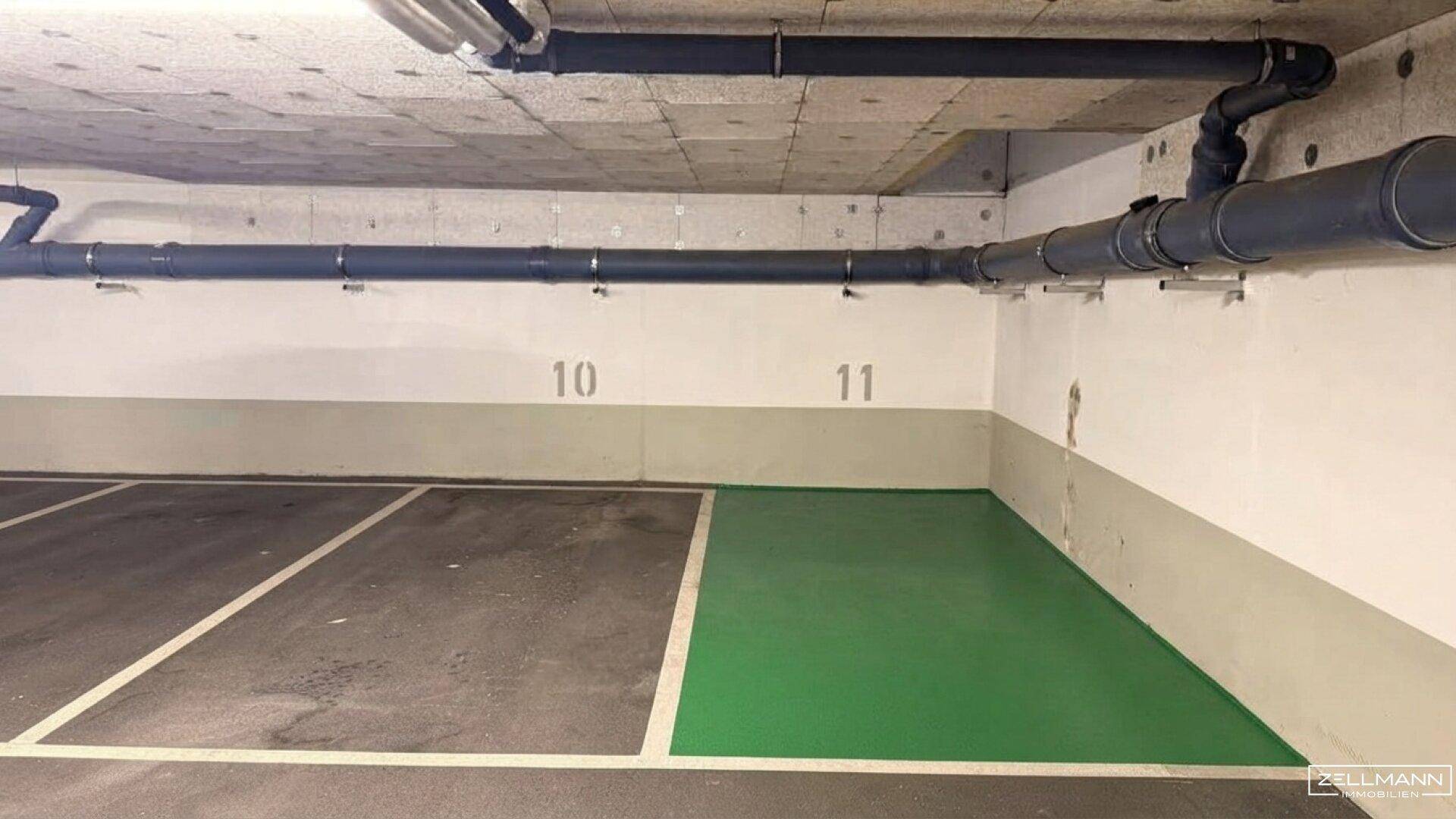 Detailansicht eines Stellplatzes in der Tiefgarage mit sichtbaren Leitungen an der Decke und grüner Markierung.