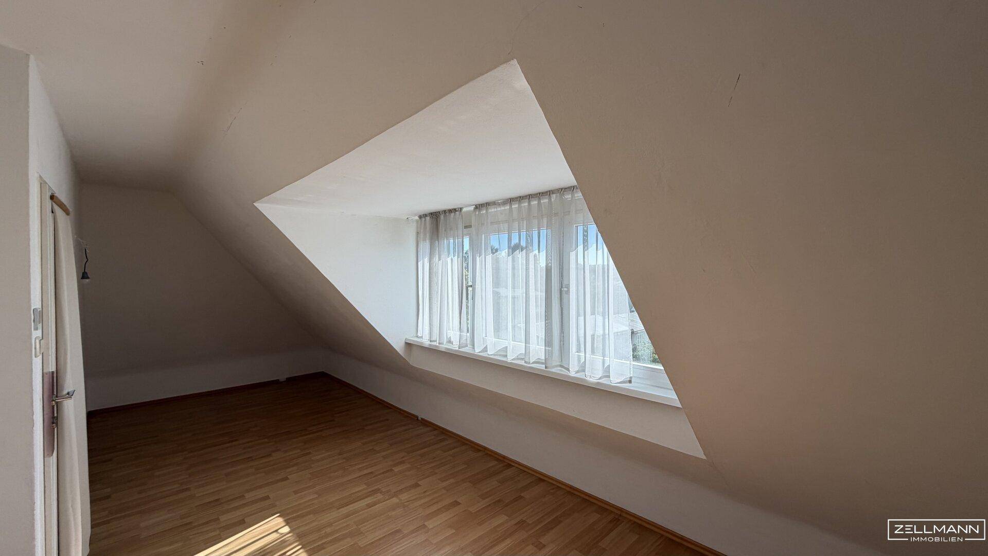 Dachzimmer mit Schrägdecke, Holzfußboden und breitem Fenster, bietet viel Helligkeit.