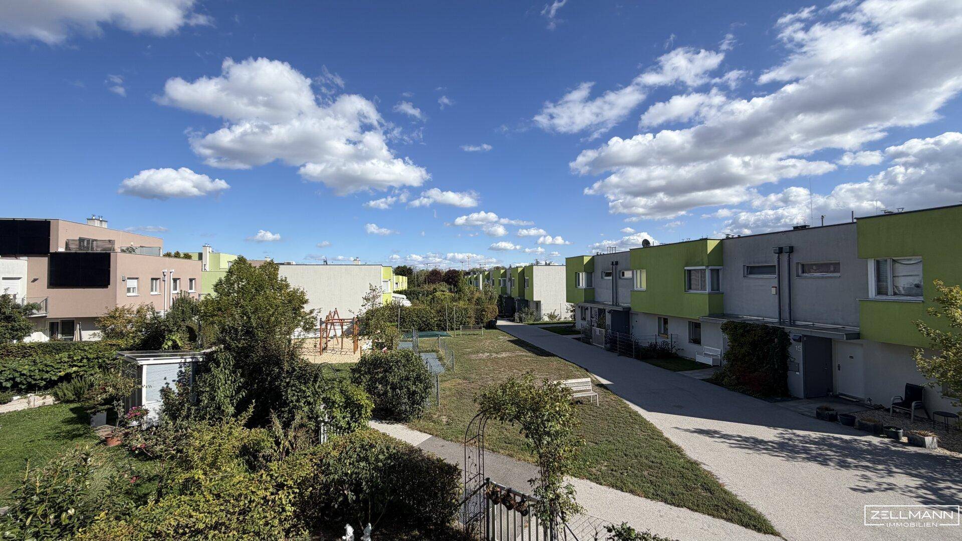 Weitläufige Grünfläche mit Spielplatz und Wegen, umgeben von modernen Wohngebäuden unter blauem Himmel.