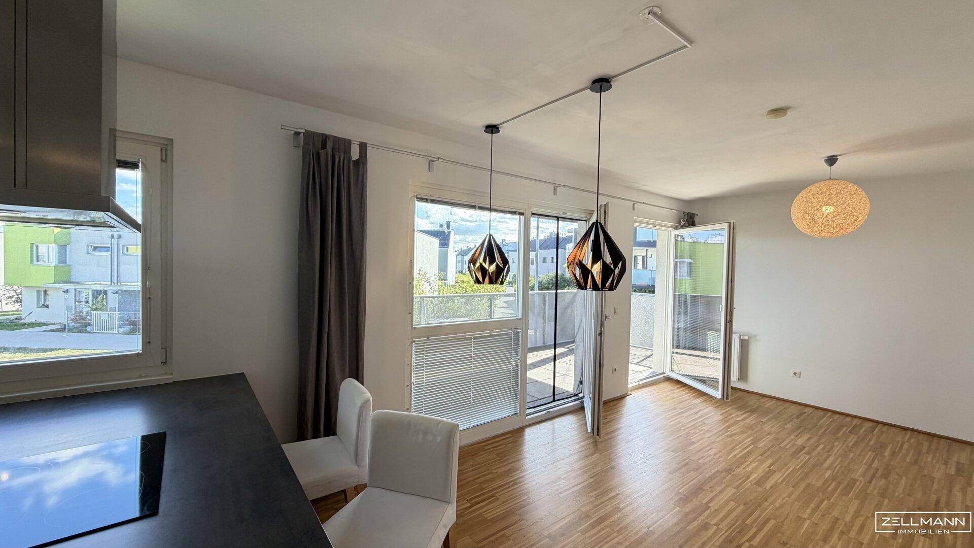 Heller Wohnbereich mit Holzboden, großen Fenstern und Zugang zu einem Balkon, modern eingerichtet.