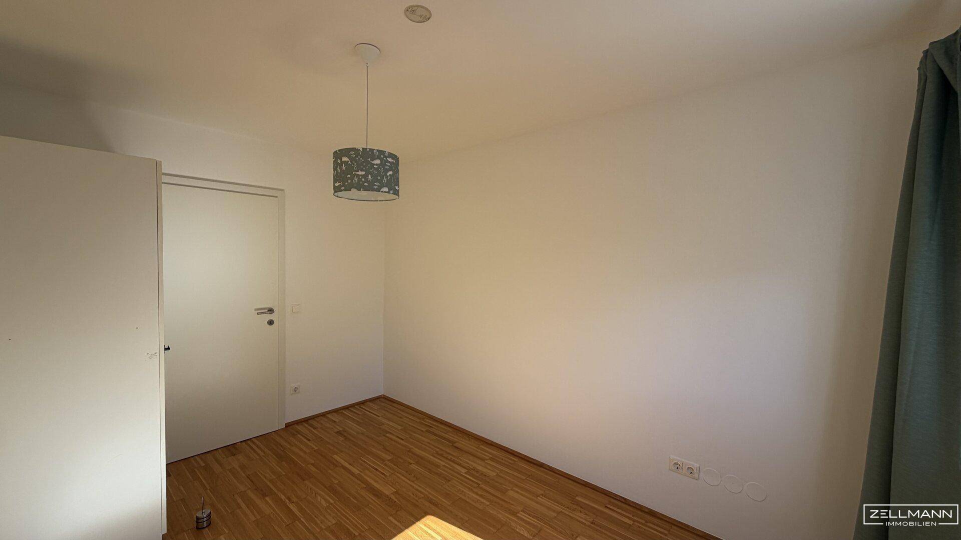 Weiterer Blick ins Schlafzimmer mit Holzboden und weißer Tür, einladend und hell gestaltet.
