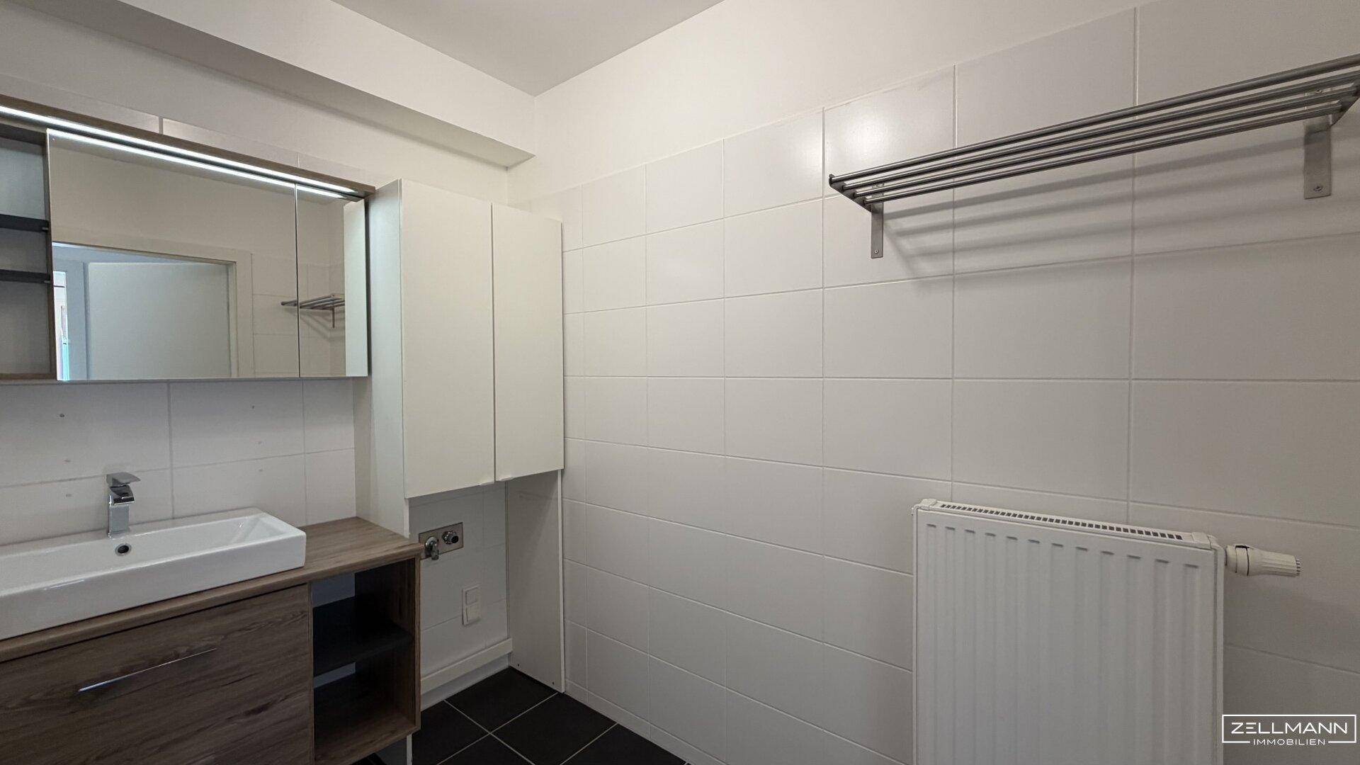 Badezimmer mit Waschtisch, Spiegelschrank und Heizkörper, ideal für Wäscheanschlüsse und Stauraum.