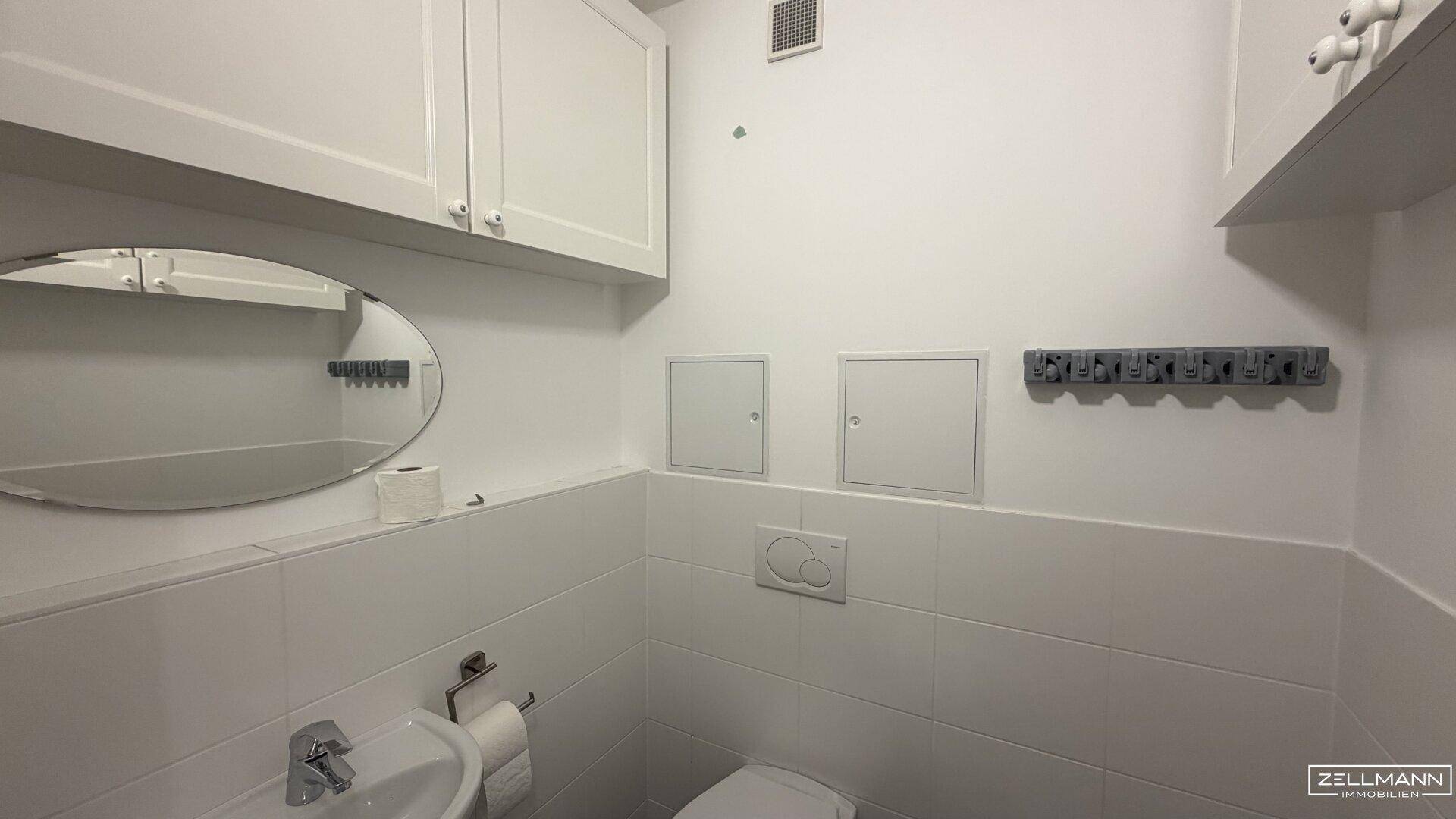 Kleines Gäste-WC mit Toilette, Waschbecken und Spiegel, praktisch und hell gefliest.