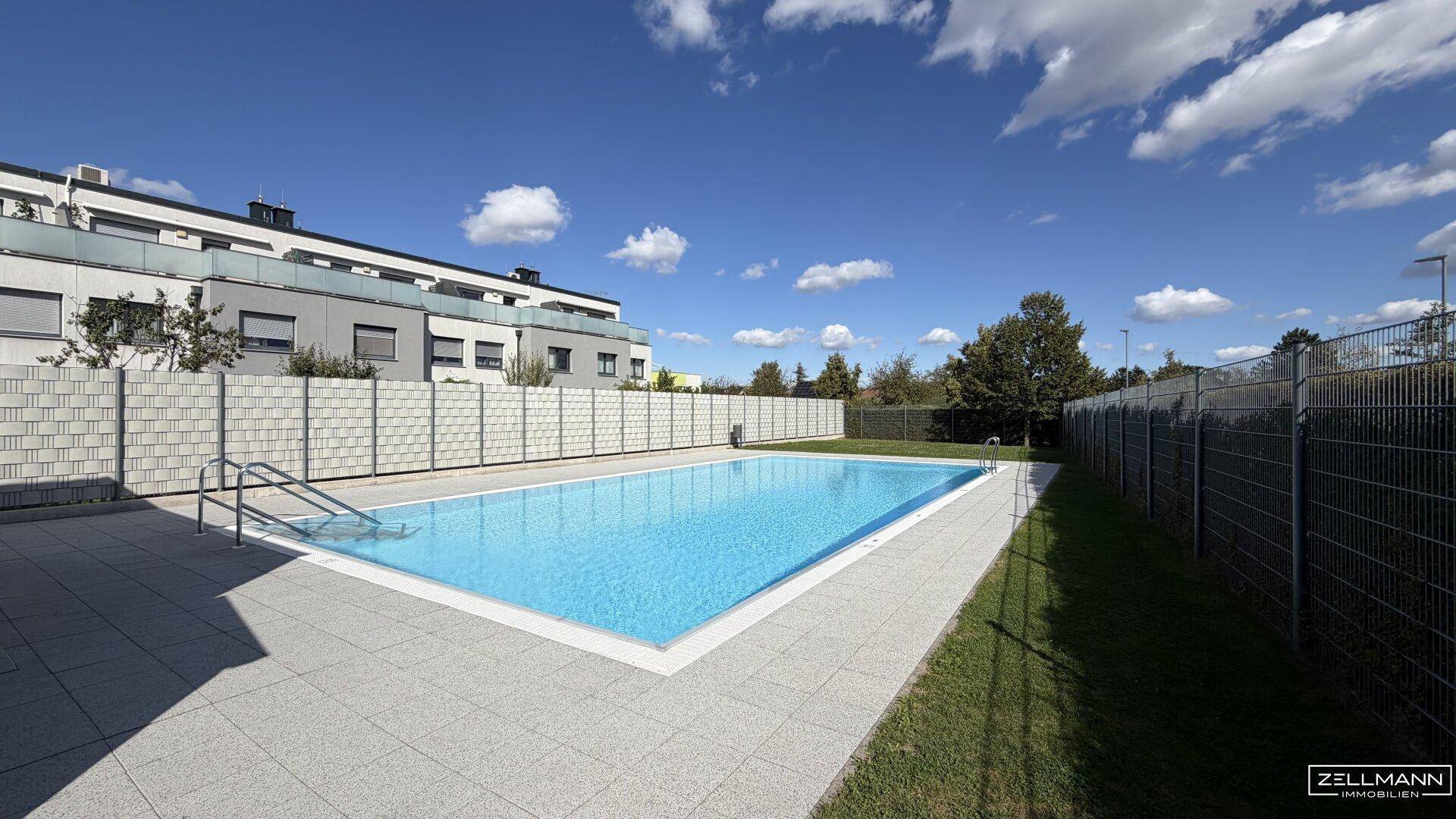 Gemeinschaftspool mit gefliester Umrandung, umgeben von Grünflächen und Wohngebäuden.