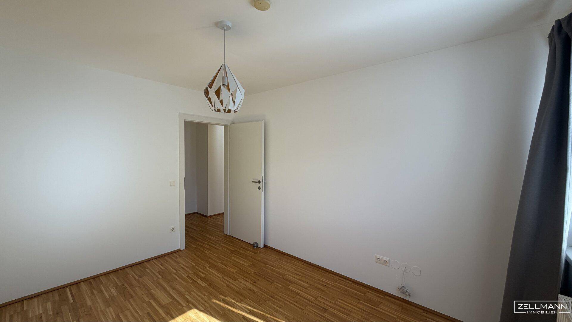 Schlafzimmer mit Holzboden und moderner Deckenleuchte, bietet direkten Zugang zu weiteren Räumen.