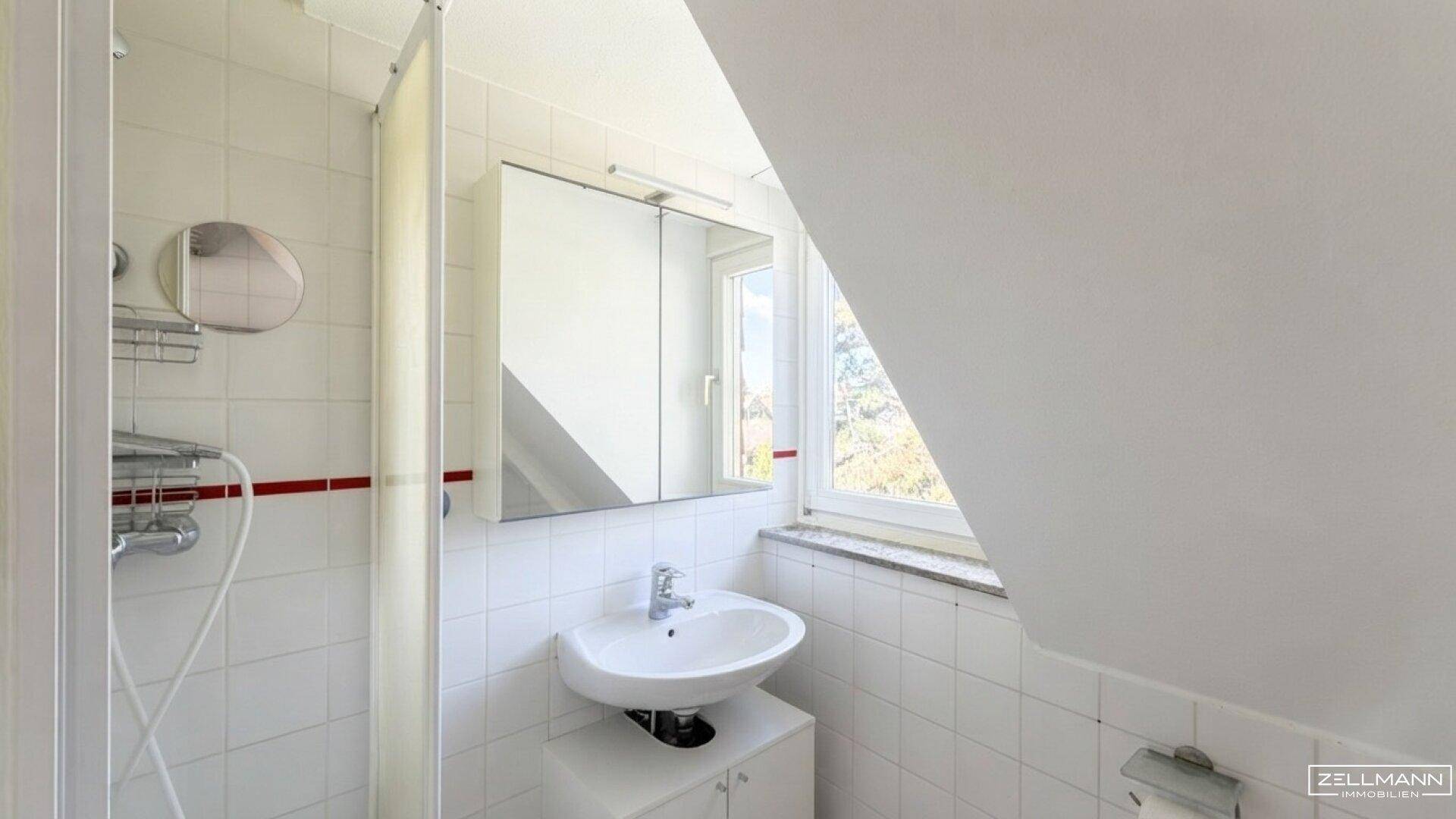 Kleines Badezimmer mit Dusche, Waschbecken und Fenster im Dachgeschoss.