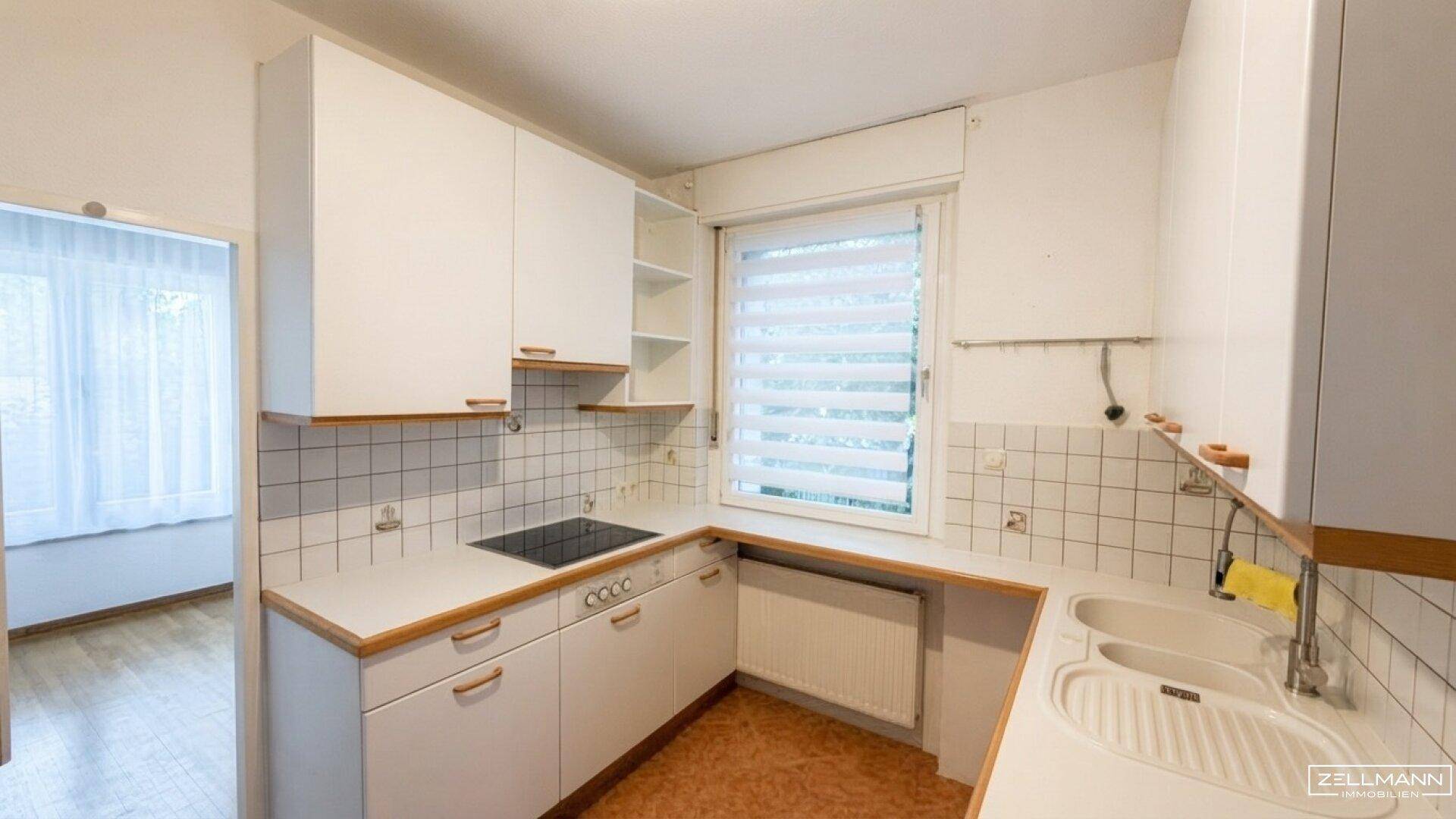 Funktionale Küche mit weißen Schränken, Fliesenrückwand und Fenster für natürliches Licht.