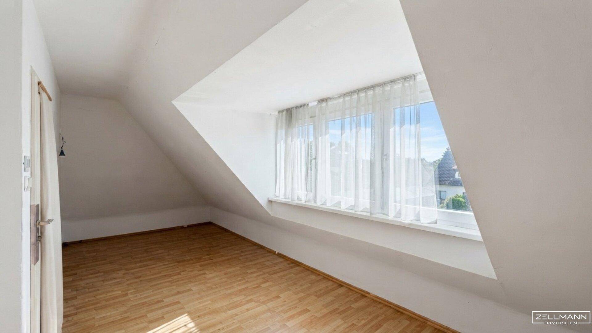 Geräumiges Dachzimmer mit Holzboden und großer Fensterfront, die viel Licht spendet.