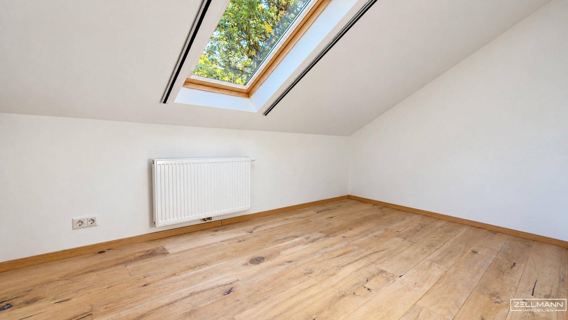 Helles Zimmer im Dachgeschoss mit Holzboden und einem großen Dachfenster für viel Tageslicht.