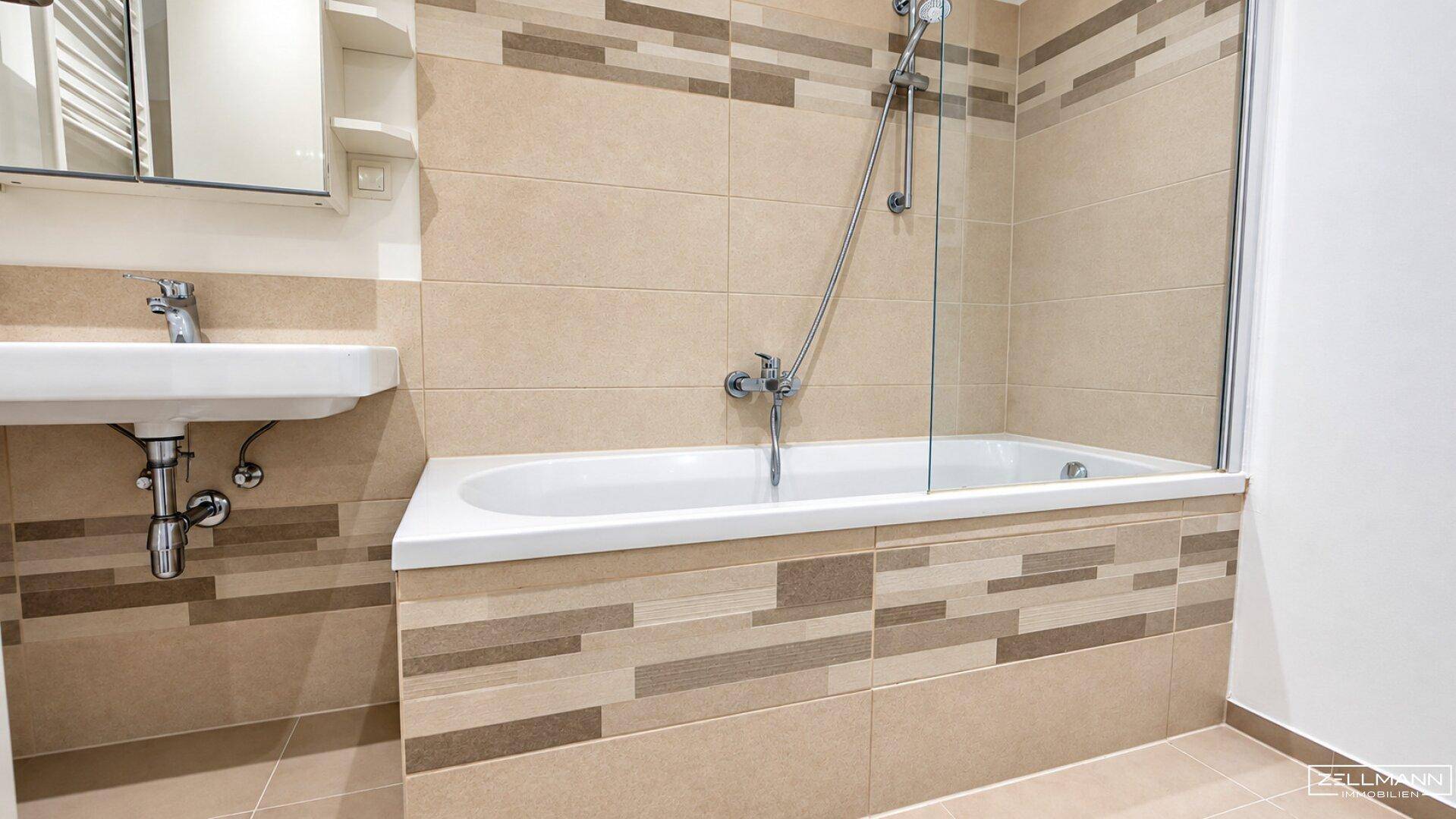 Modernes Badezimmer mit Badewanne, Duschfunktion und beigefarbenen Fliesen.