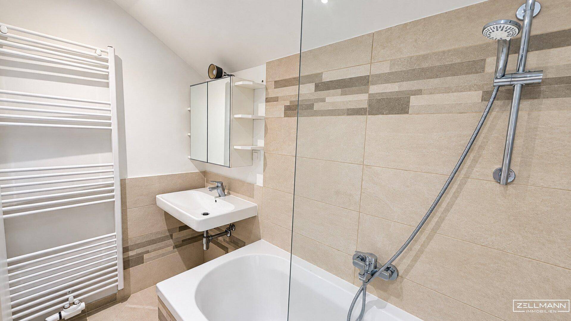Helles Badezimmer mit Badewanne, Duschvorrichtung, Waschbecken und beheiztem Handtuchhalter.