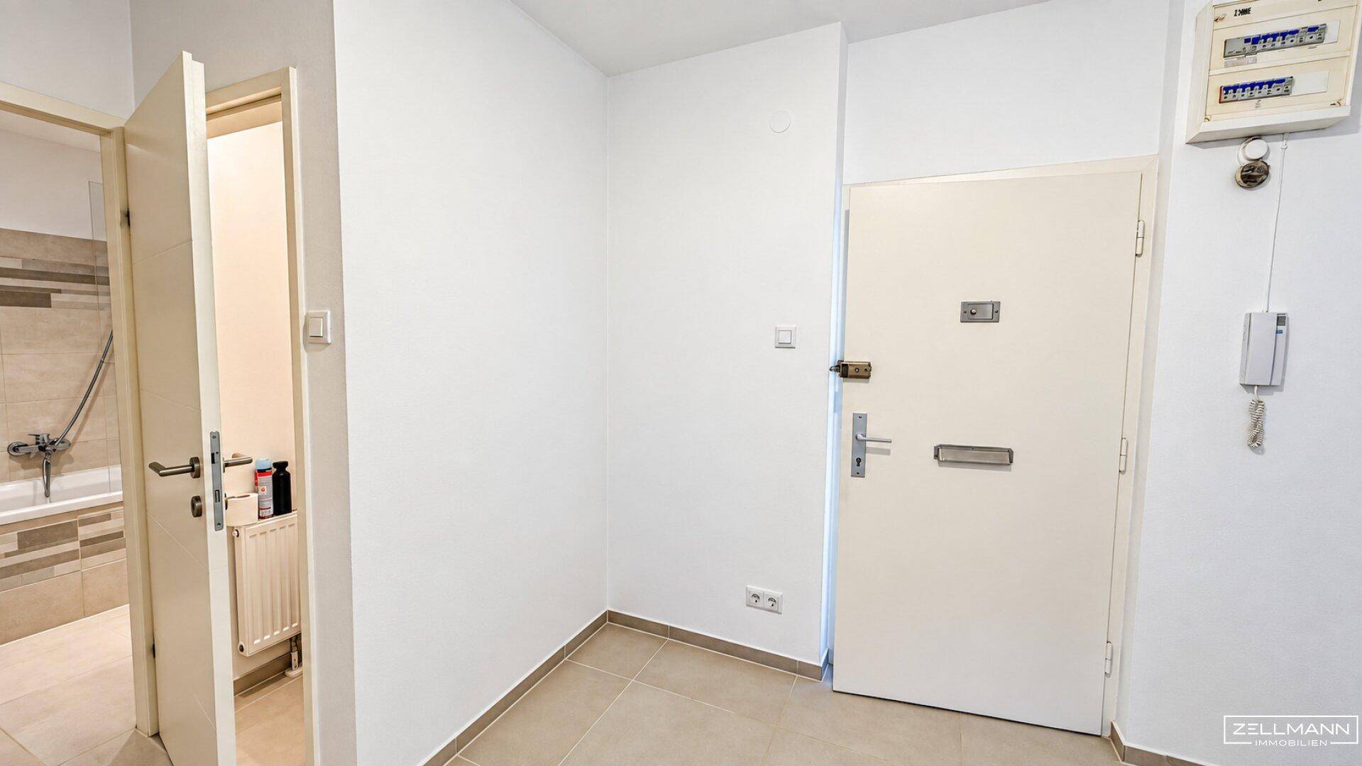Eingangsbereich mit heller Fliese, Sicherheitstür und Zugang zum Badezimmer.