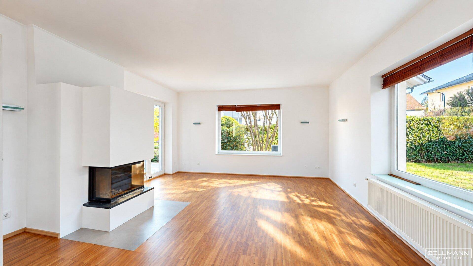 Helles Wohnzimmer mit Kamin, Parkettboden und großen Fenstern zum Garten.