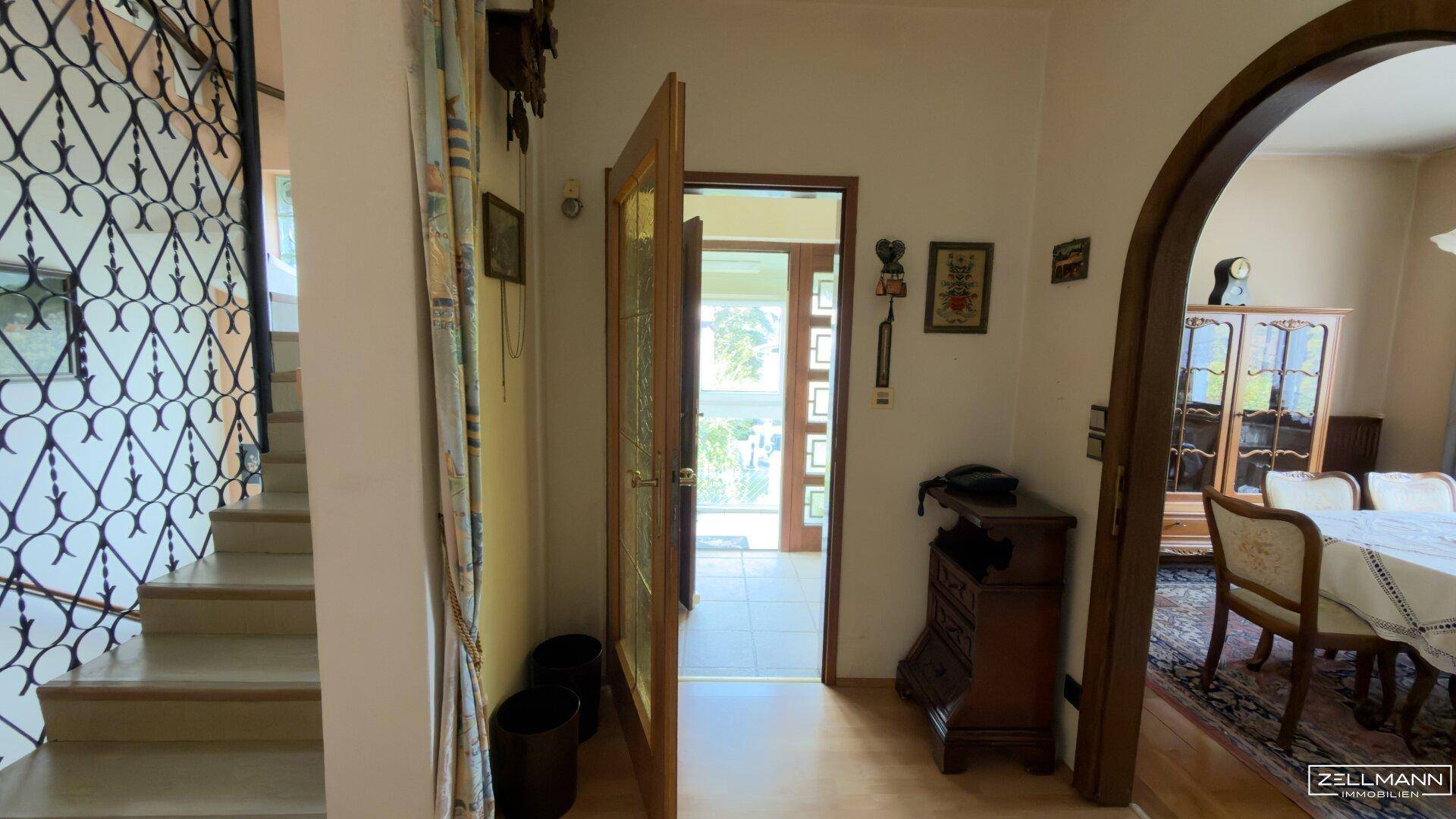 Geräumiger Eingangsbereich mit Treppe, schmiedeeisernem Geländer und Blick zum Esszimmer.