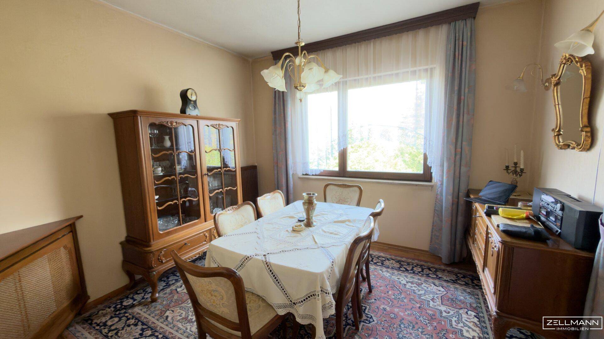 Gemütliches Esszimmer mit traditionellen Holzmöbeln, einem Kronleuchter und Blick ins Grüne.