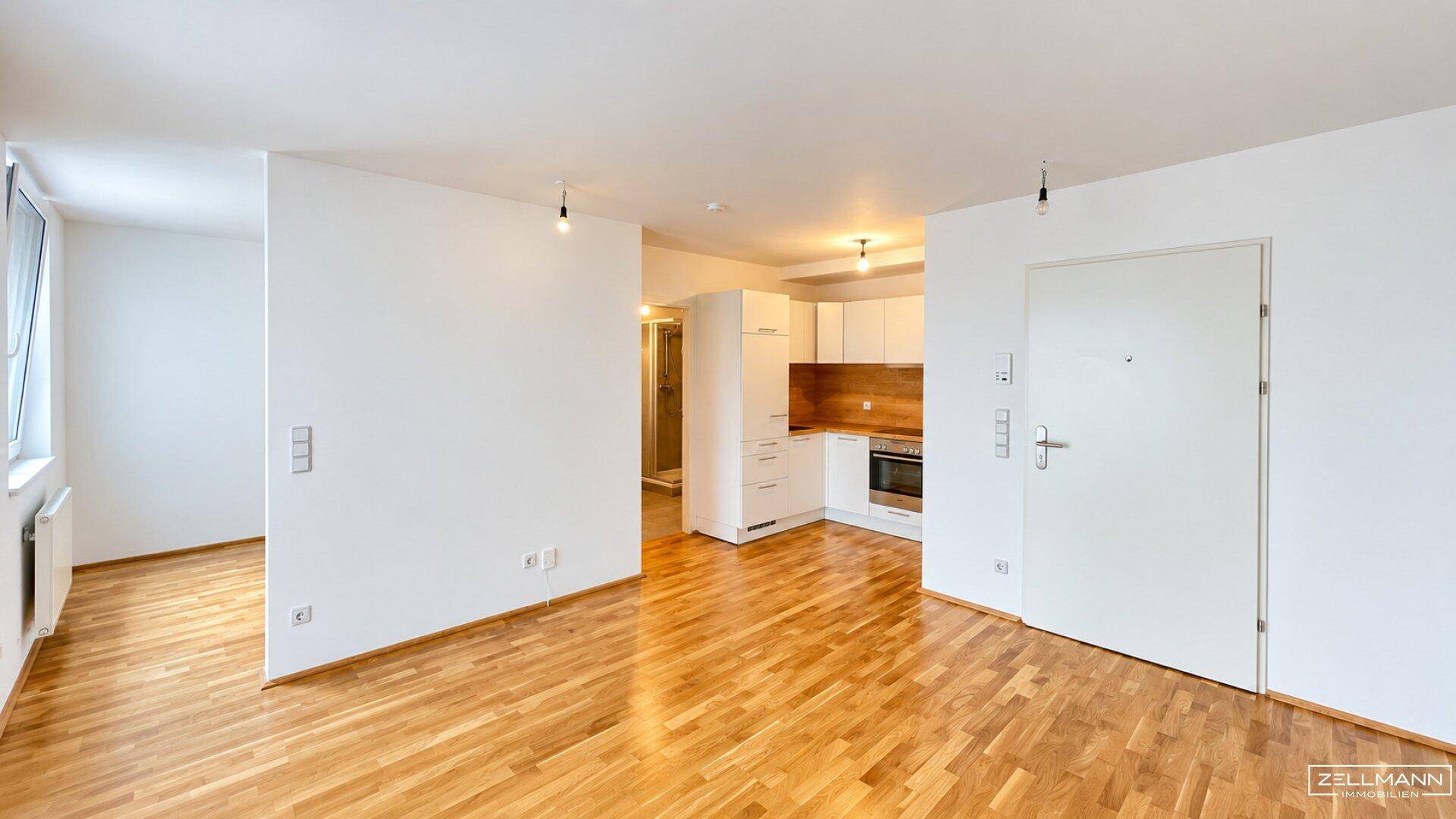 Heller offener Wohnbereich mit Holzparkettboden und Blick auf die integrierte Küche.