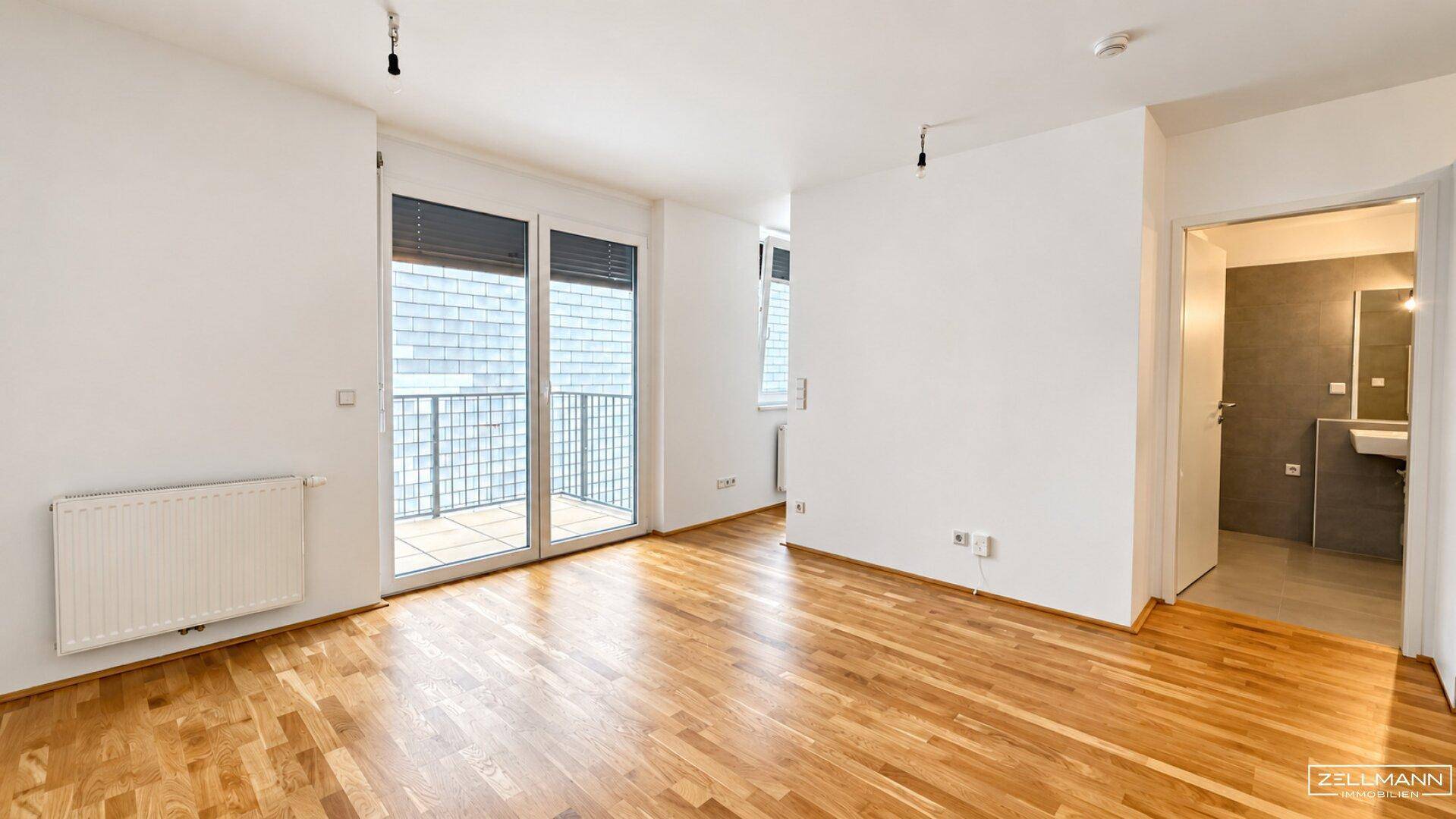 Geräumiges Wohnzimmer mit Parkettboden, Heizkörper und Zugang zu einem französischen Balkon.