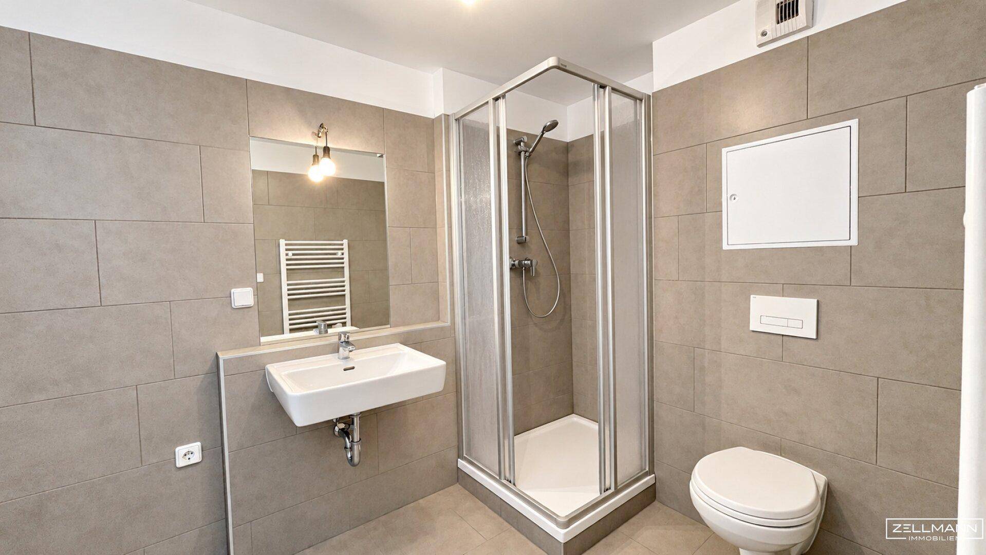 Modernes Badezimmer mit grauen Fliesen, Duschkabine, wandhängendem WC und Handtuchheizkörper.