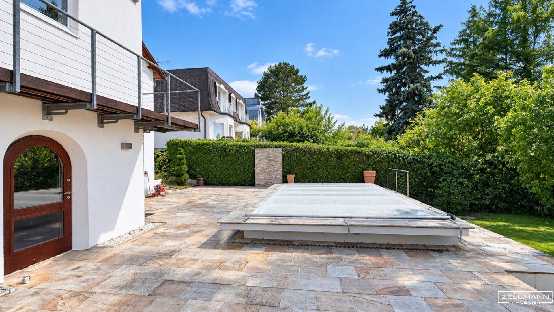 Geräumige Steinterrasse mit Poolabdeckung und Blick auf den grünen Gartenbereich.