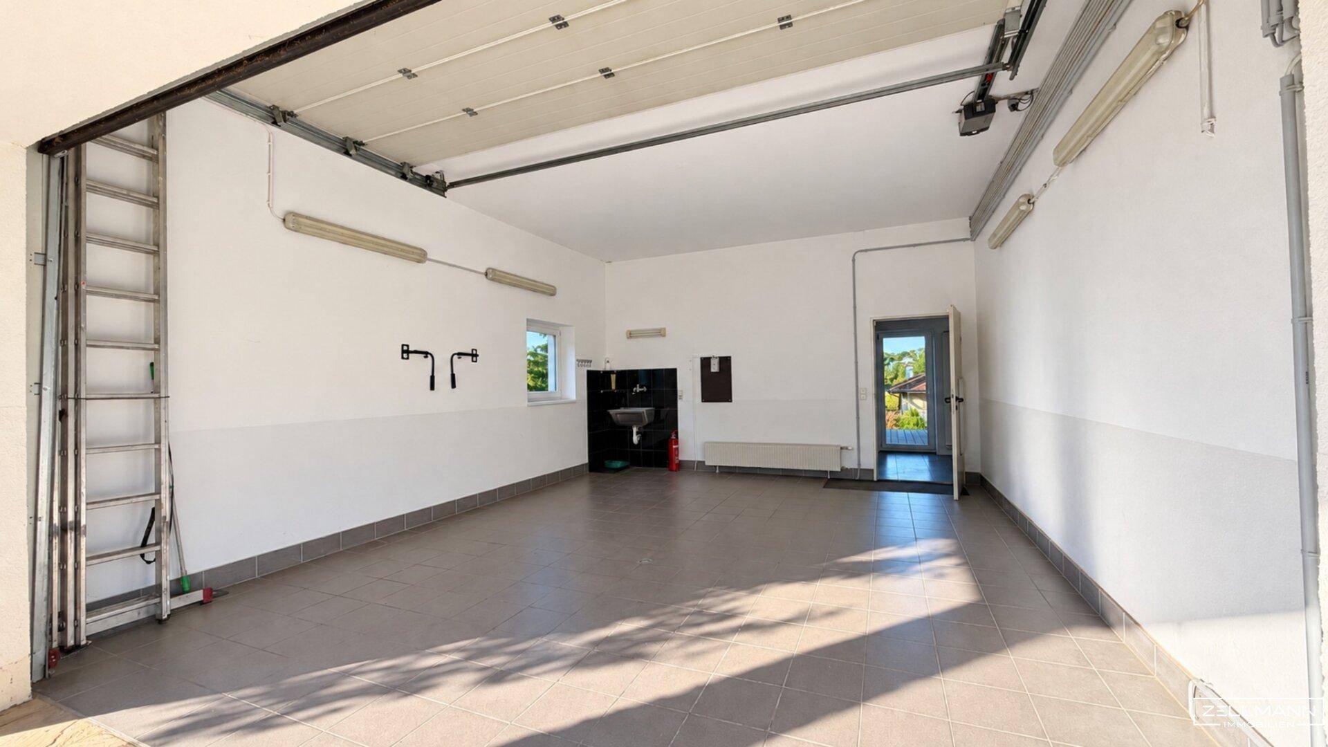 Geräumige Garage mit Fliesenboden, Rolltor und Tageslichtfenster.
