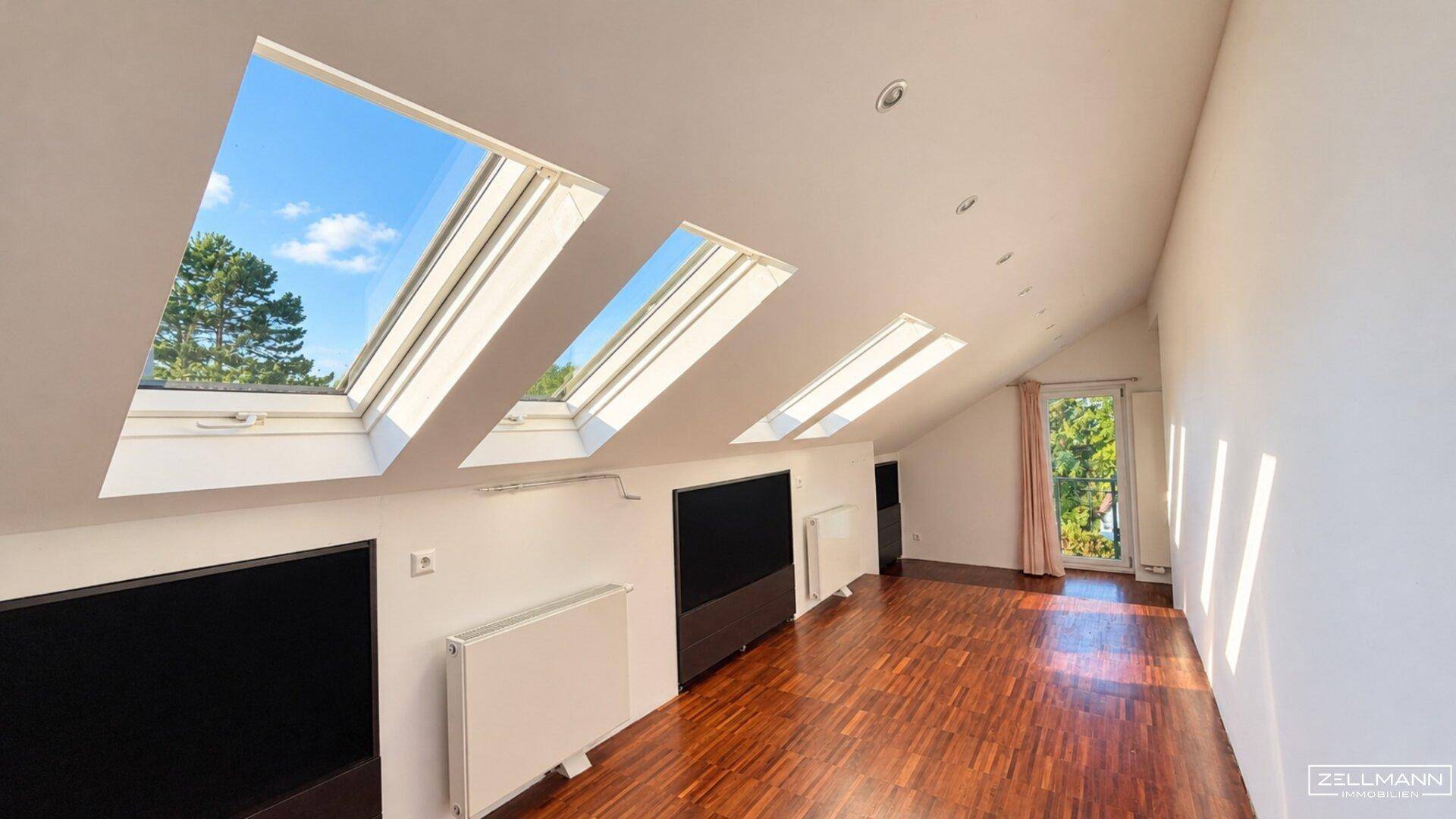Dachgeschossraum mit Holzboden, schrägen Decken und mehreren Dachfenstern.