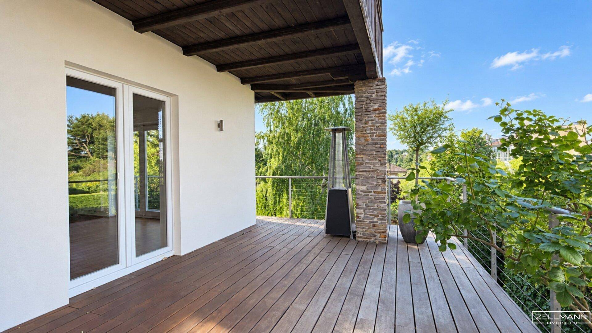 Geräumiger Holzbalkon mit Heizstrahler und Blick auf die grüne Umgebung.