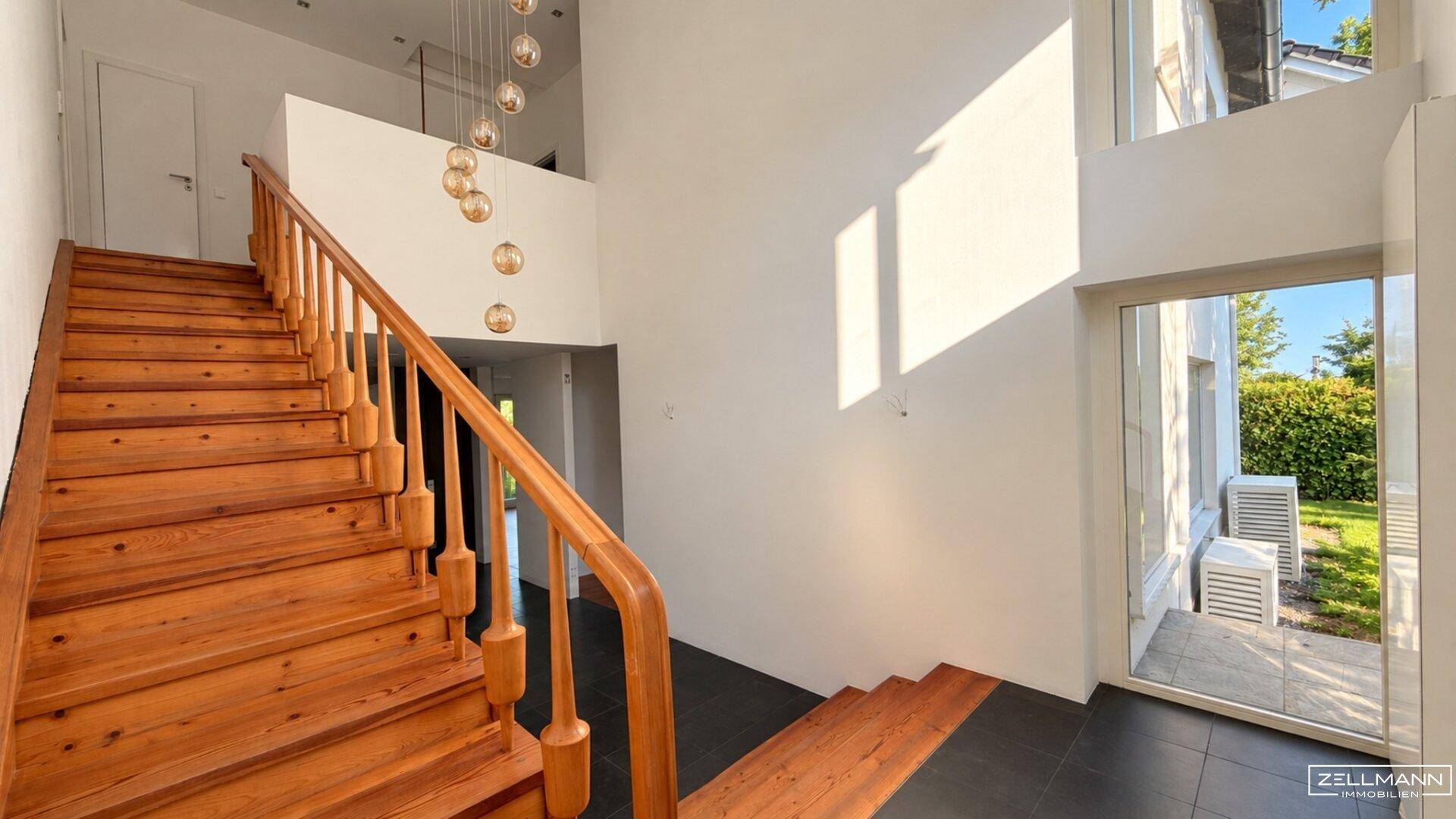 Heller Eingangsbereich mit Holztreppe, hohen Decken und modernen Hängelampen.