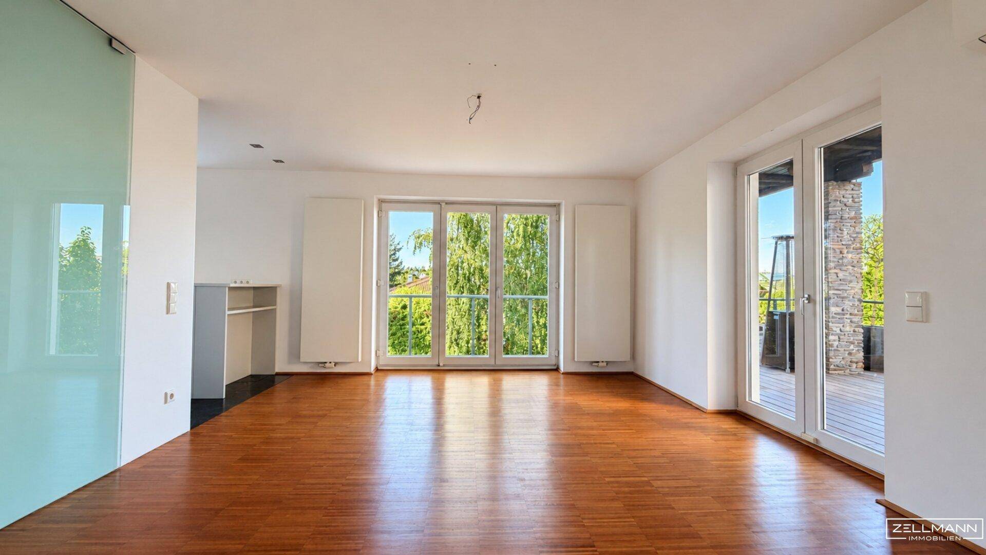 Helles Wohnzimmer mit Holzboden und großen Fenstertüren, die viel Licht hereinlassen.