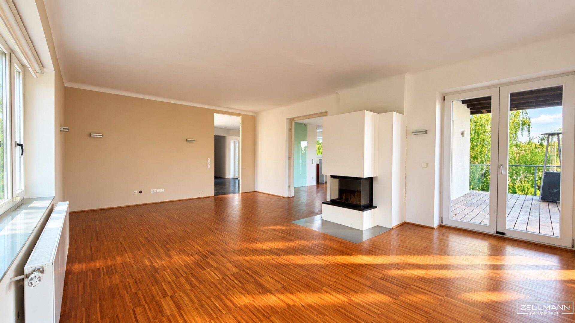Großes Wohnzimmer mit Parkettboden, Kamin und Zugang zu einem Balkon.