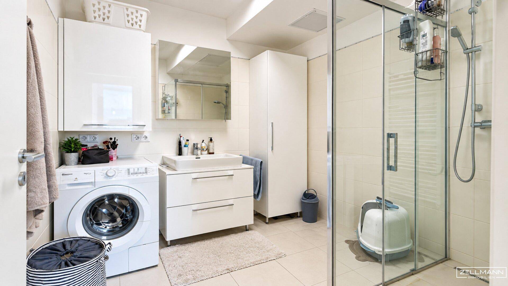 Helles Badezimmer mit Duschkabine, Waschmaschine, Waschbecken und Spiegelschrank.
