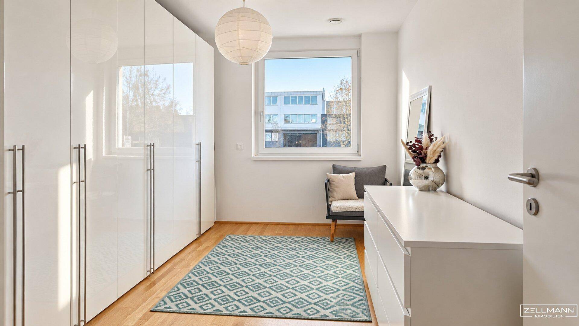 Helles Schlafzimmer mit großen weißen Kleiderschränken, Holzboden und Fensterblick.