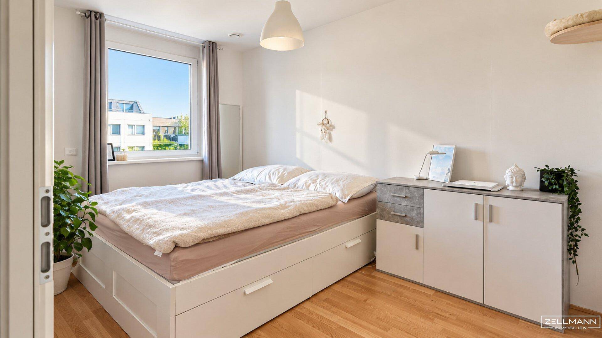 Gemütliches Schlafzimmer mit Doppelbett, Holzboden und viel Tageslicht durch das Fenster.