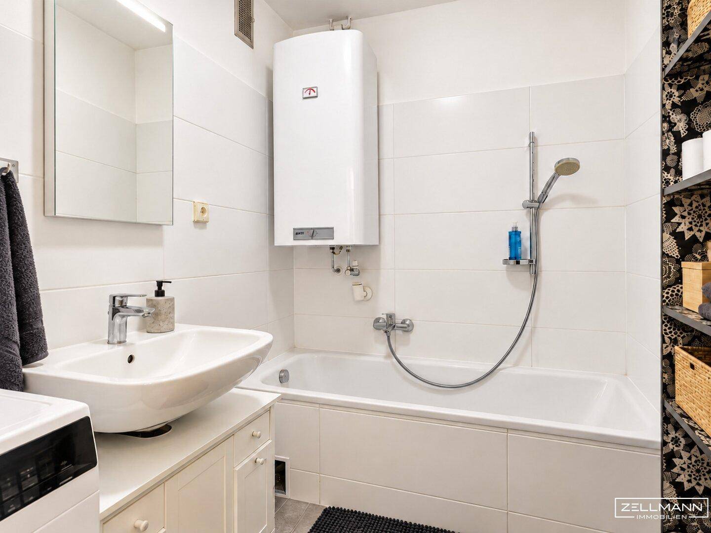Funktionales Badezimmer mit weißen Fliesen, Badewanne mit Duschfunktion und einem Warmwasserboiler.