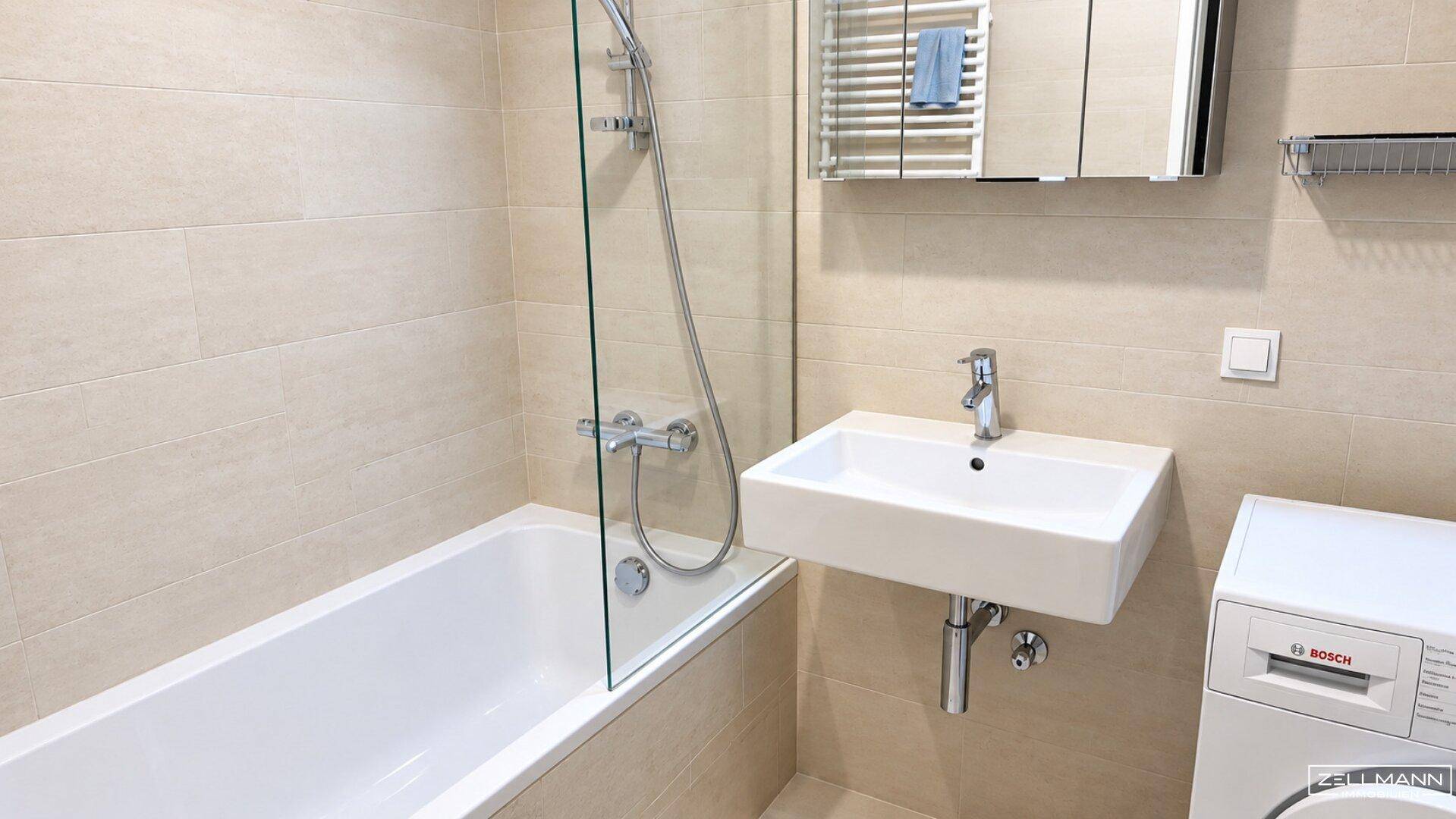 Funktionales Badezimmer mit Badewanne, Dusche, Waschbecken und integrierter Waschmaschine.