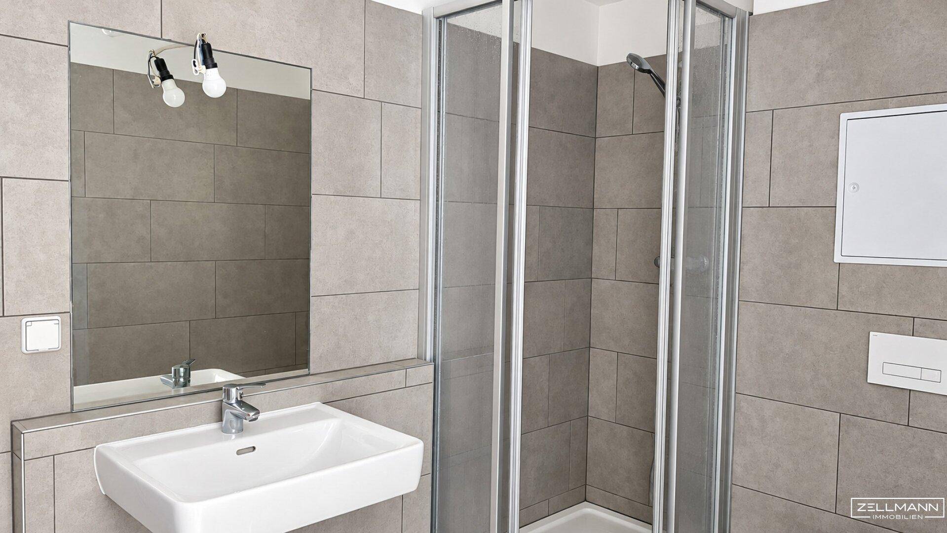 Modernes Badezimmer mit grauen Fliesen, Einzelwaschbecken und einer praktischen Duschkabine.