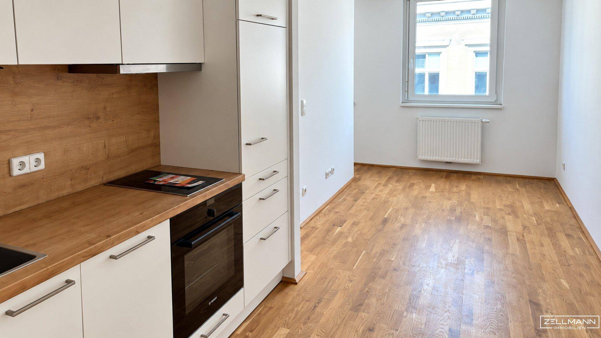 Moderne Küchenzeile mit Holzarbeitsplatte, Induktionskochfeld und Backofen in einem offenen Wohnbereich.