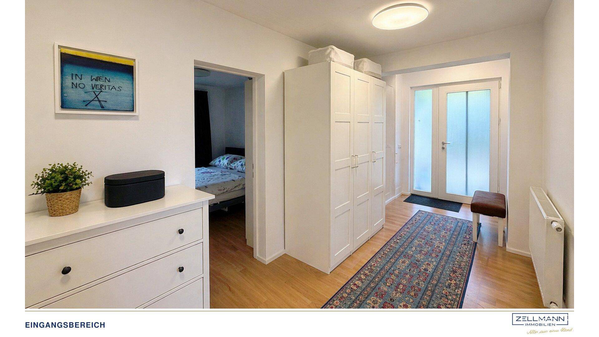 Eingangsbereich mit Holzfußboden, weißem Kleiderschrank und Zugang zu einem weiteren Zimmer.