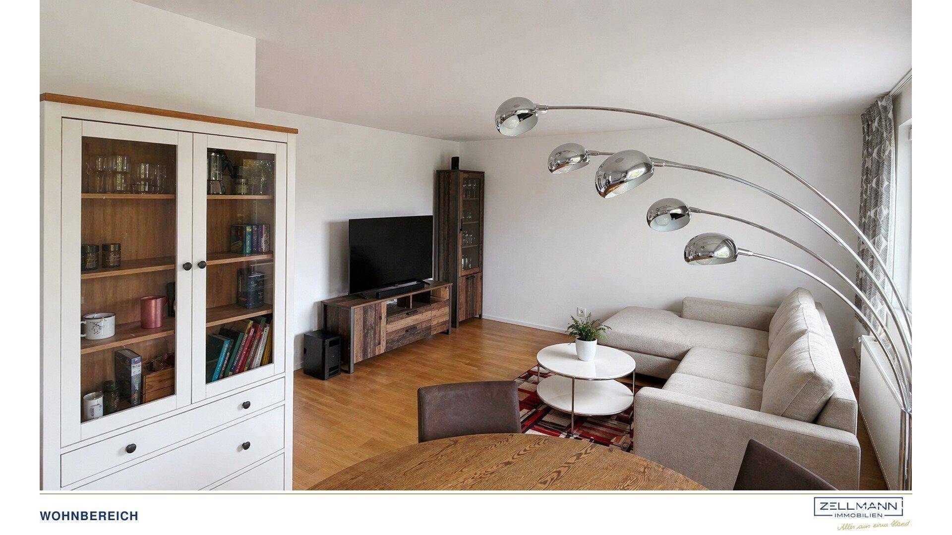 Heller Wohnbereich mit beigem Sofa, Fernseher und einer modernen Stehlampe.