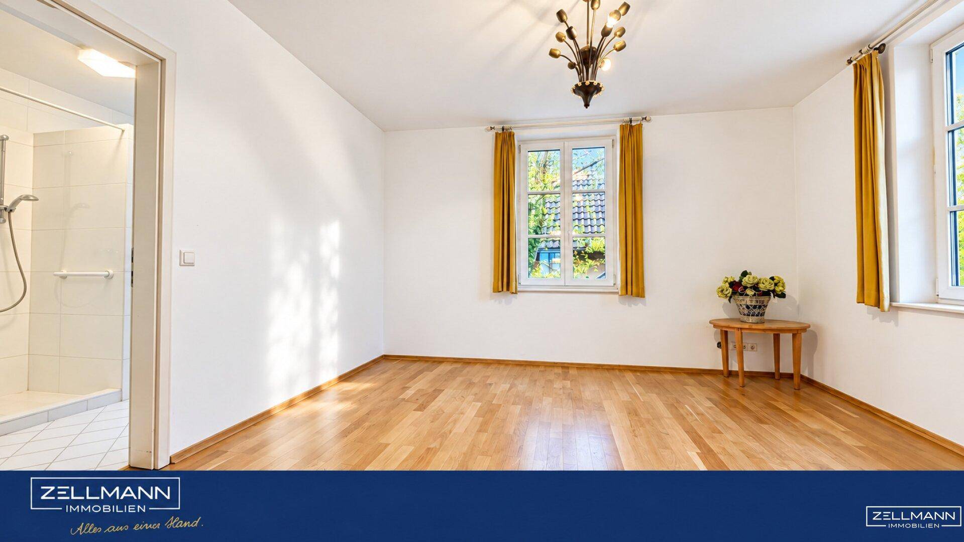 Helles Schlafzimmer mit Parkettboden, Fenster und Zugang zu einem Badezimmer.