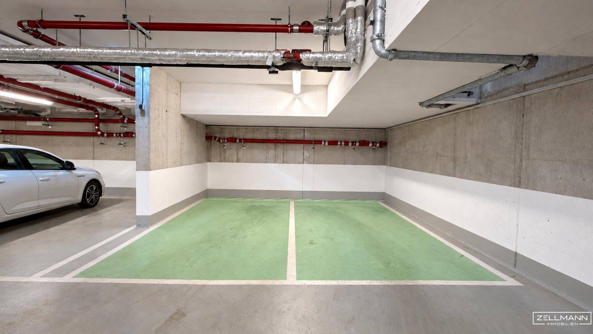 Tiefgaragenstellplatz mit markierter Parkfläche und sichtbaren Installationen an der Decke.