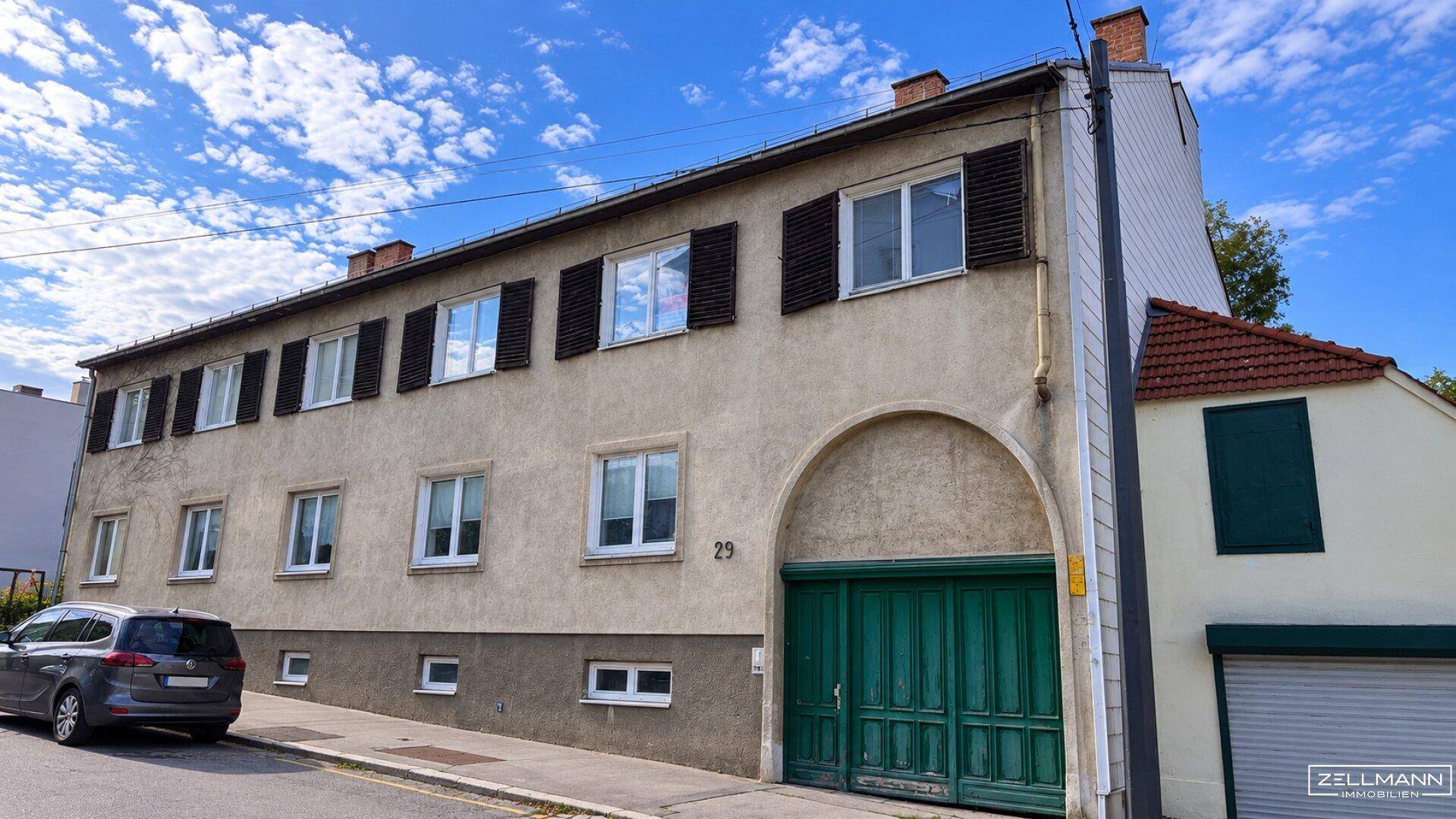Straßenansicht eines Wohnhauses mit grüner Garagentür und Fensterläden.