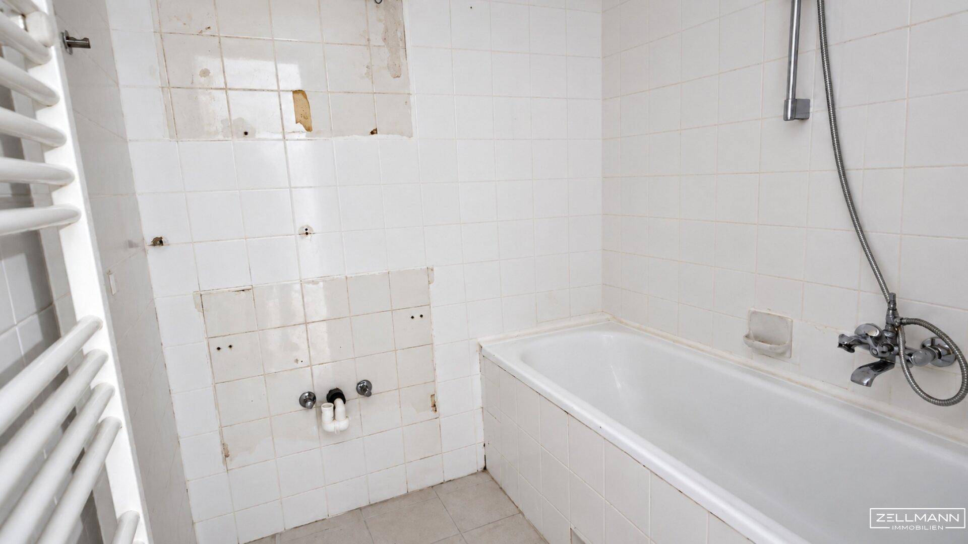 Badezimmer in Renovierung mit weiß gefliesten Wänden, Badewanne und Heizkörper für Handtücher.