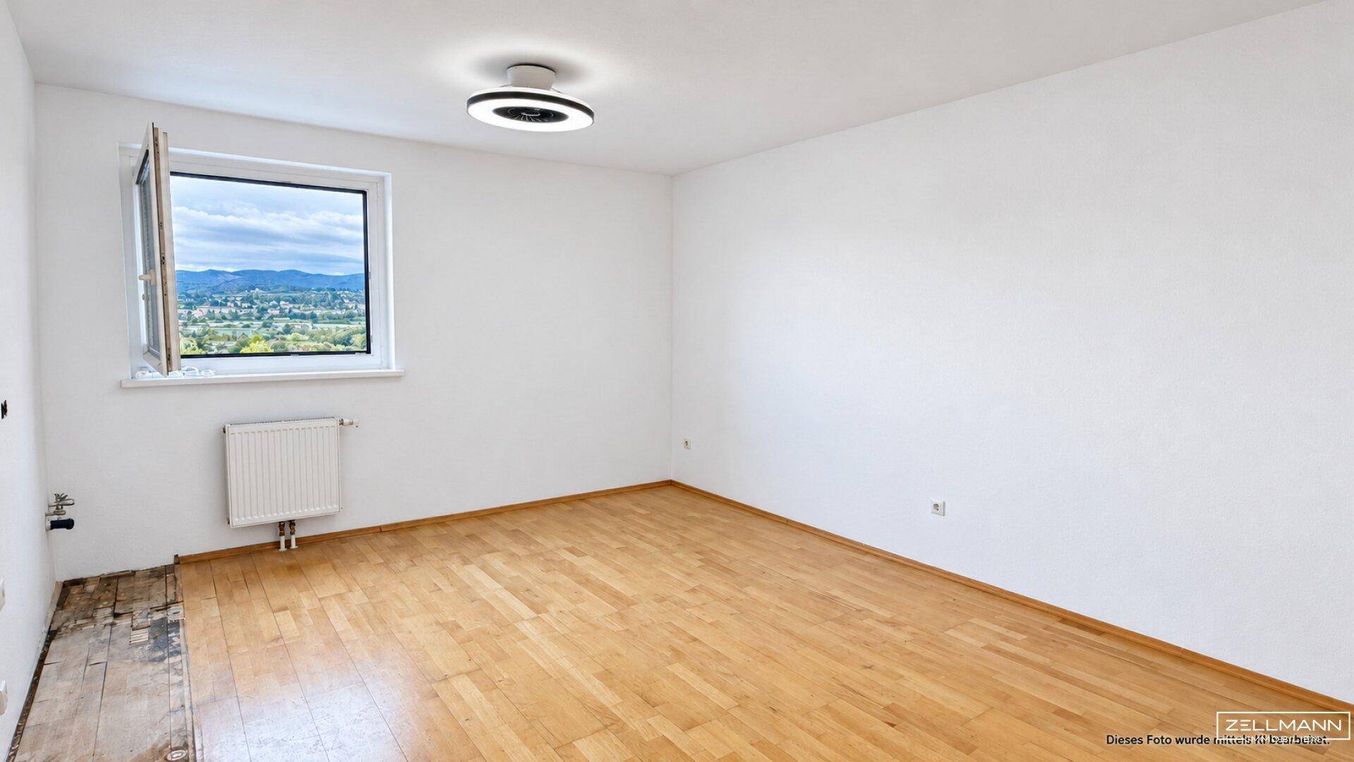 Helles, leeres Zimmer mit Parkettboden, weißen Wänden und einem Fenster mit Bergblick.