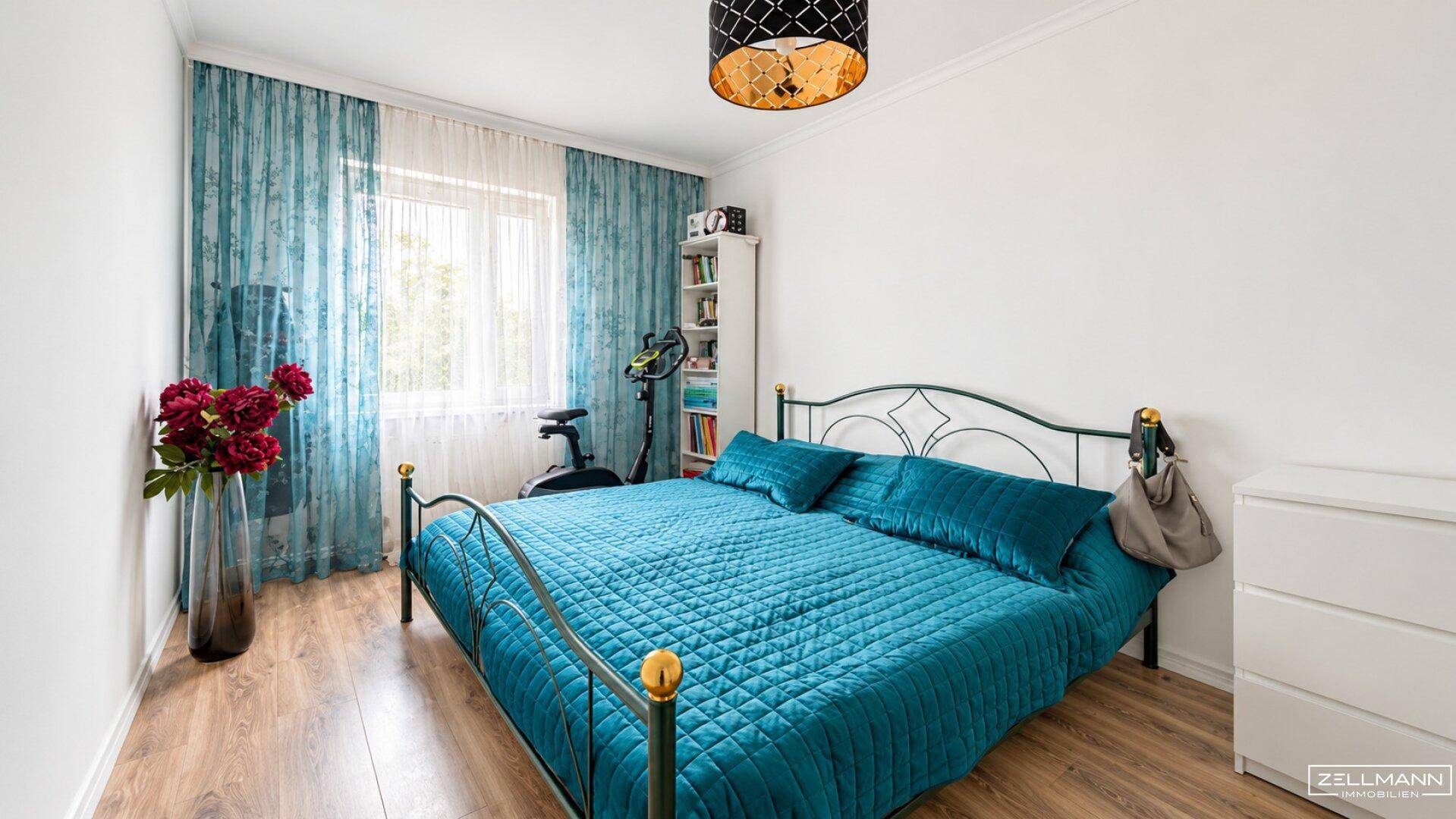 Schlafzimmer mit Doppelbett, blauer Bettwäsche, Holzboden und großen Fenstern.
