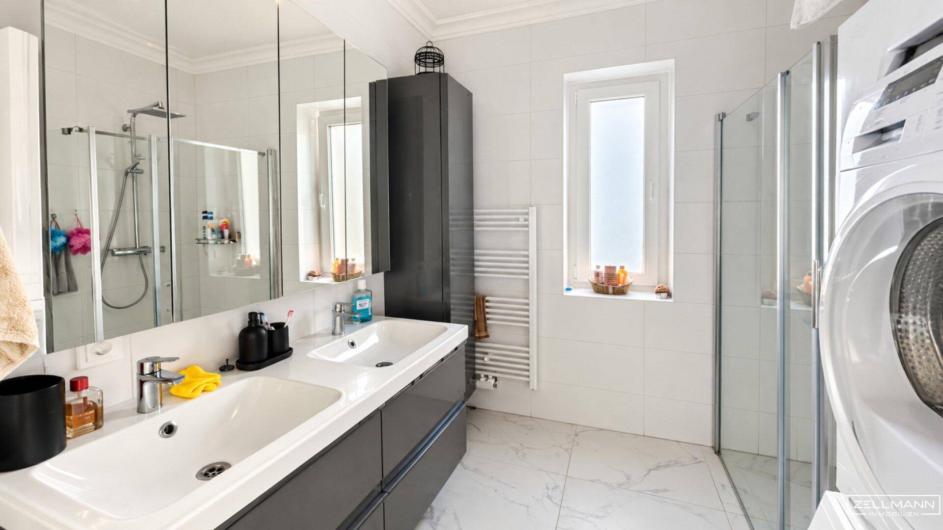 Modernes Badezimmer mit Doppelwaschbecken, Dusche, Fenster und Waschmaschine.