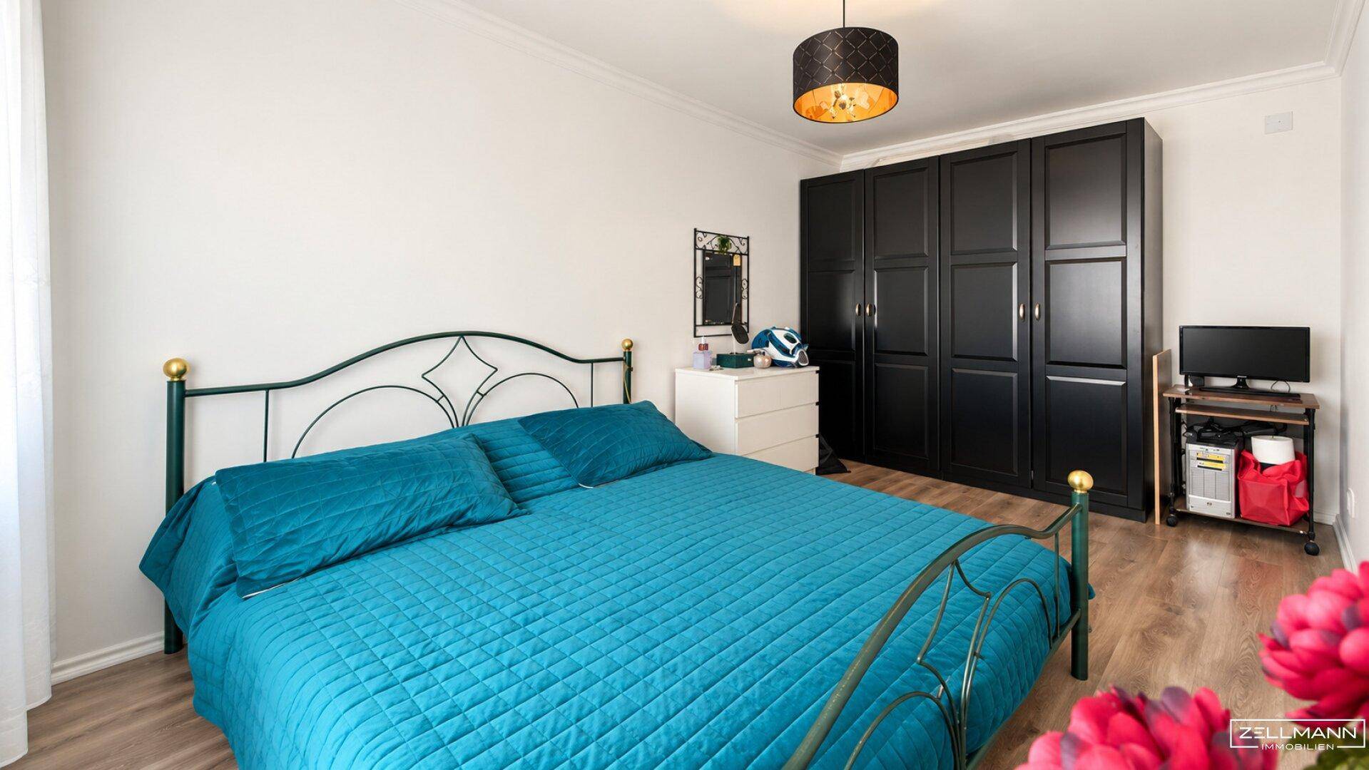 Schlafzimmer mit Doppelbett, schwarzem Kleiderschrank und Holzboden.