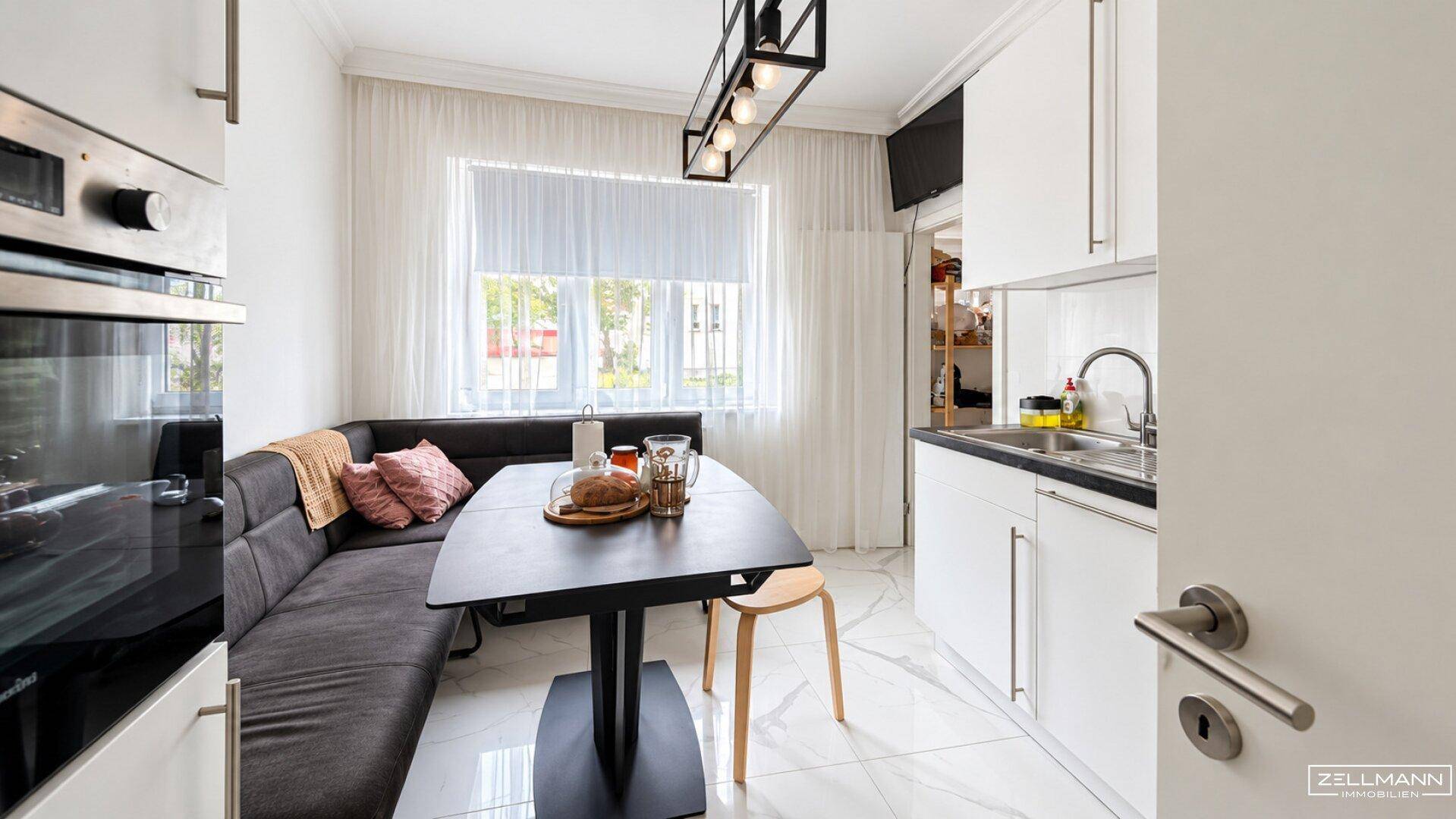 Moderne Küche mit weißer Einbauküche, Essbereich und Fenster mit Vorhängen.